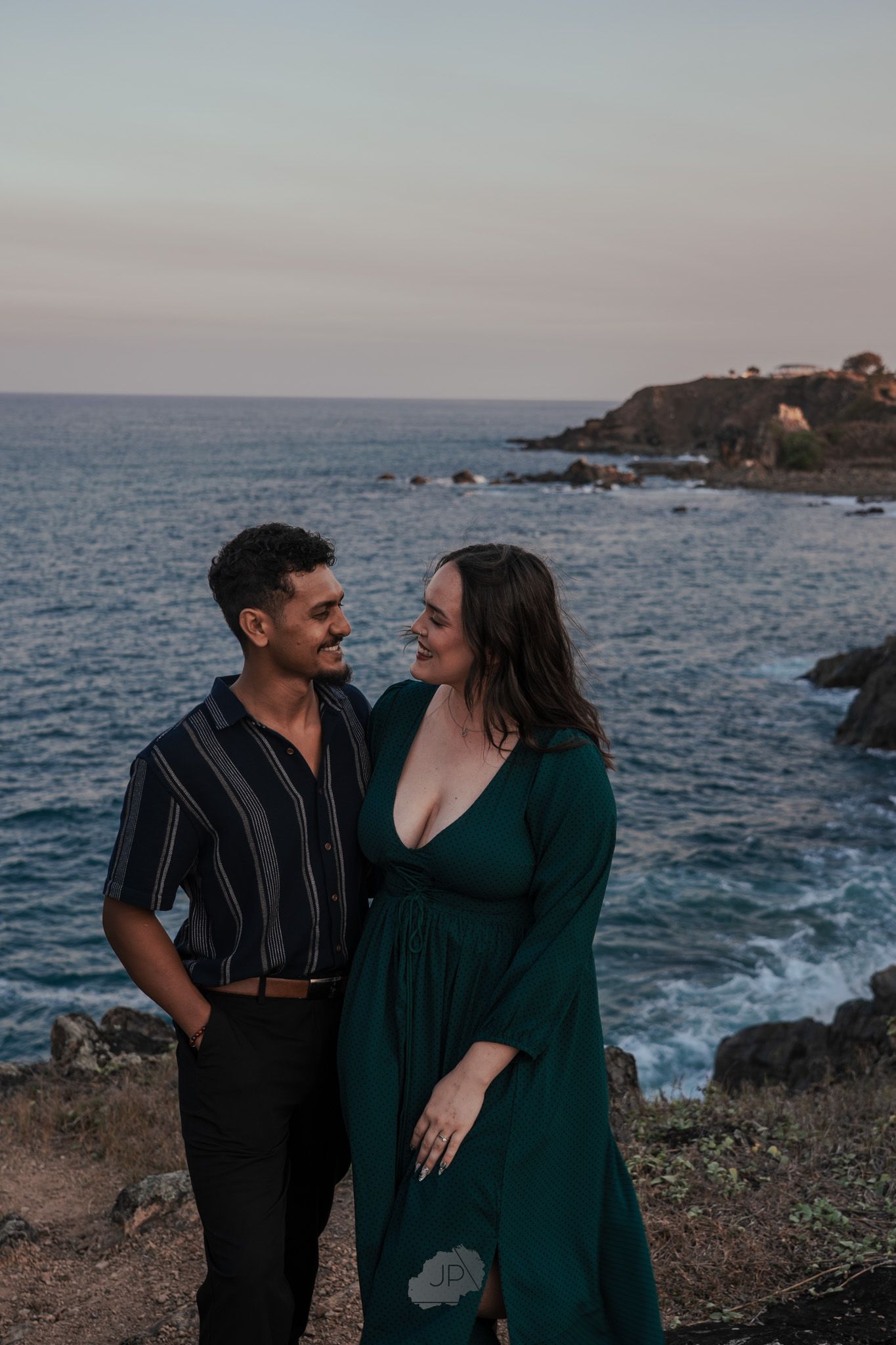 A couple shares romantic moments together on a scenic coastal cliff overlooking the ocean at sunset.