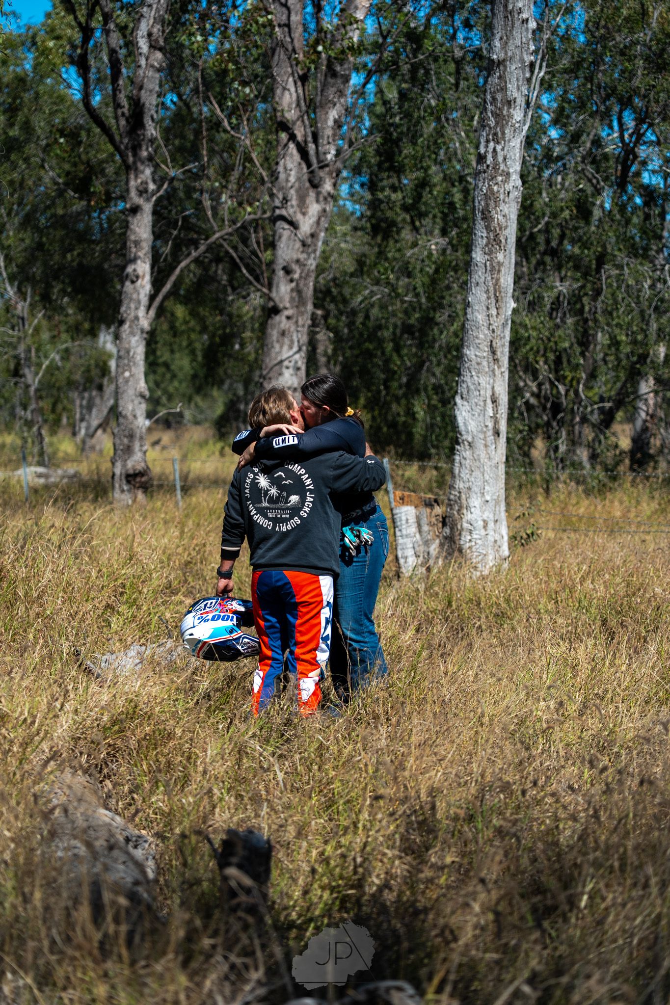 Two people sitting together on a grassy hillside among tall eucalyptus trees in a peaceful outdoor setting.
