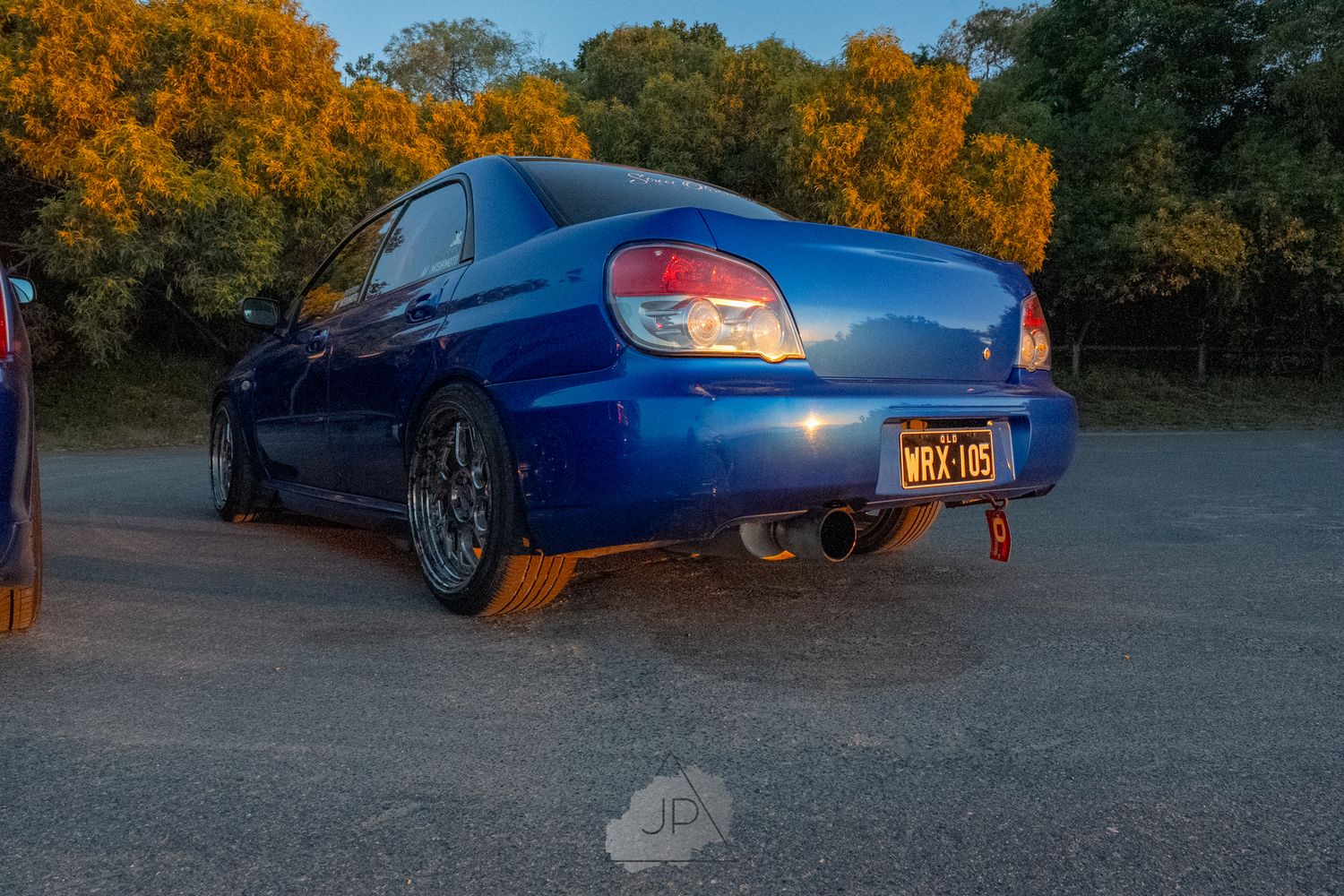 Blue Subaru WRX sports car drifting on road with autumn foliage in background during sunset.