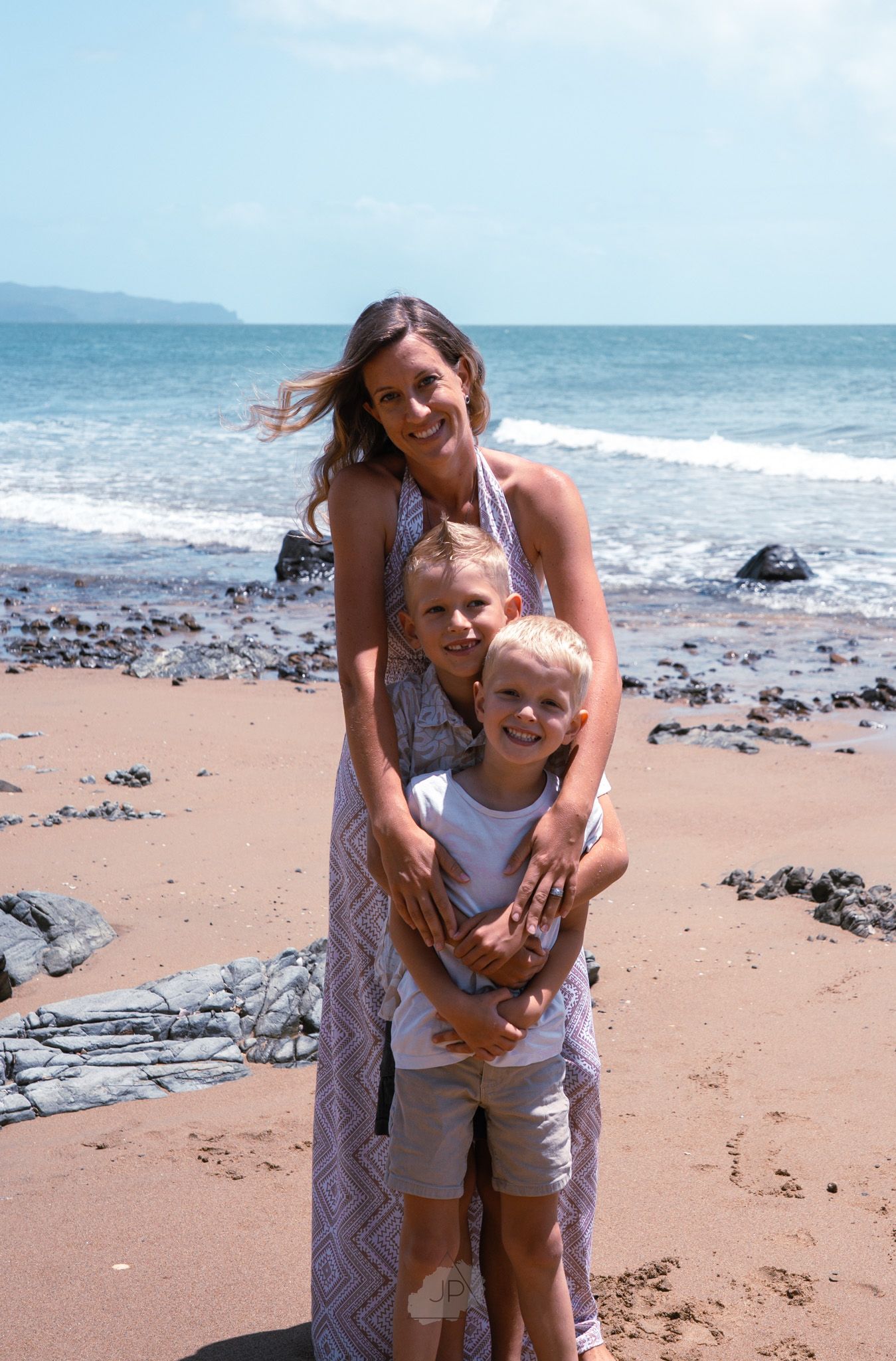 A joyful moment captured at a sunny beach with waves and rocks visible in the background.