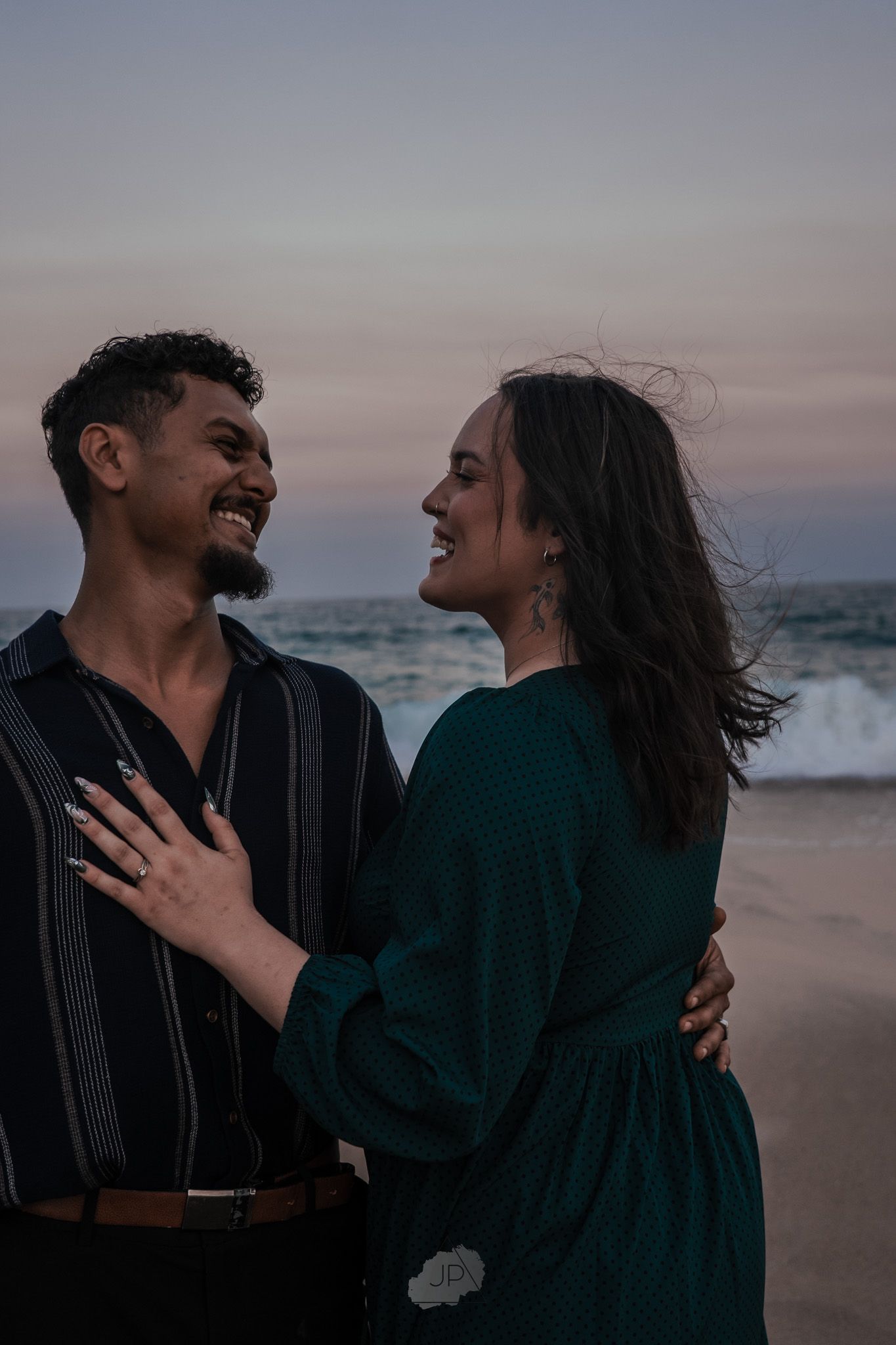 A couple shares joyful laughter together during a romantic sunset photoshoot at the beach.