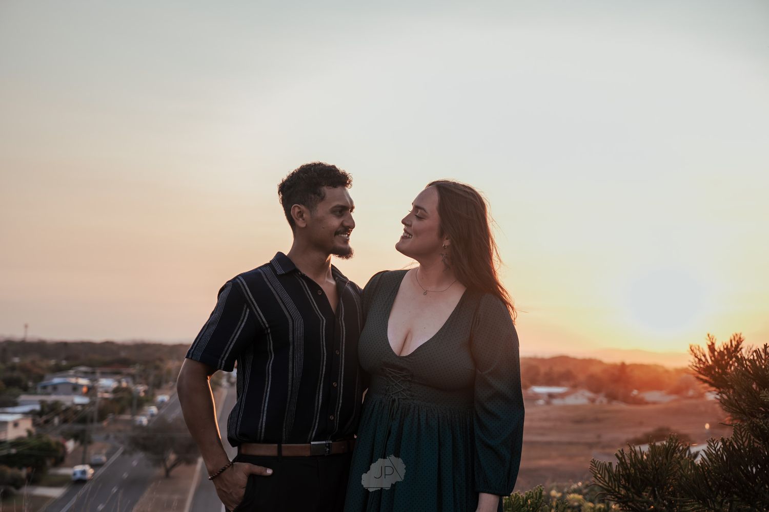 Couple embraces on a hilltop against a glowing sunset backdrop while sharing an intimate moment together.