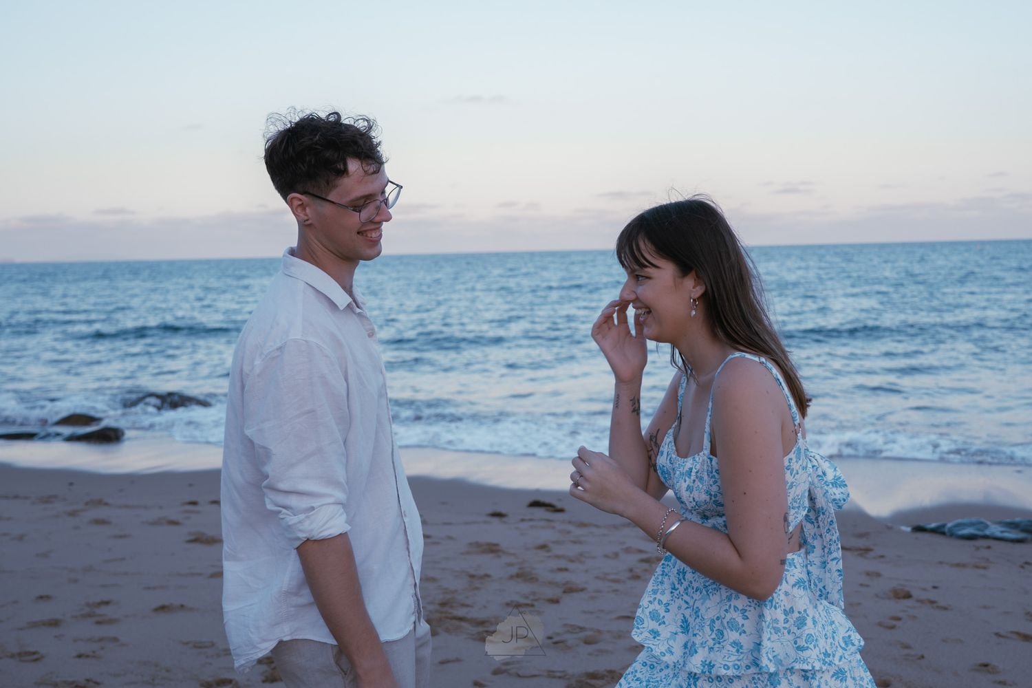 Couple shares romantic moments on a beach at sunset with ocean waves in the background.