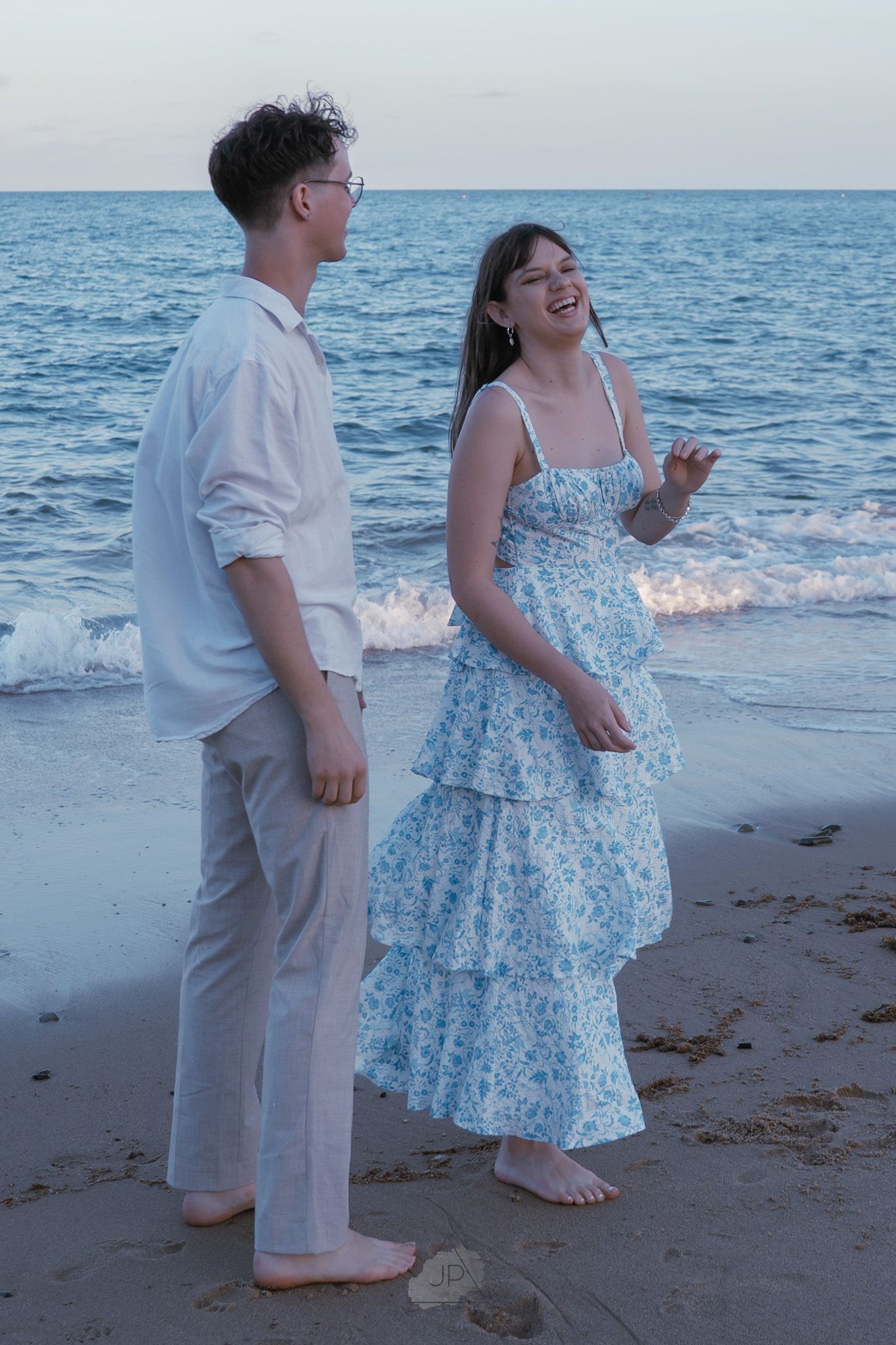 A couple shares a romantic moment at sunset on a beach with waves crashing behind them.