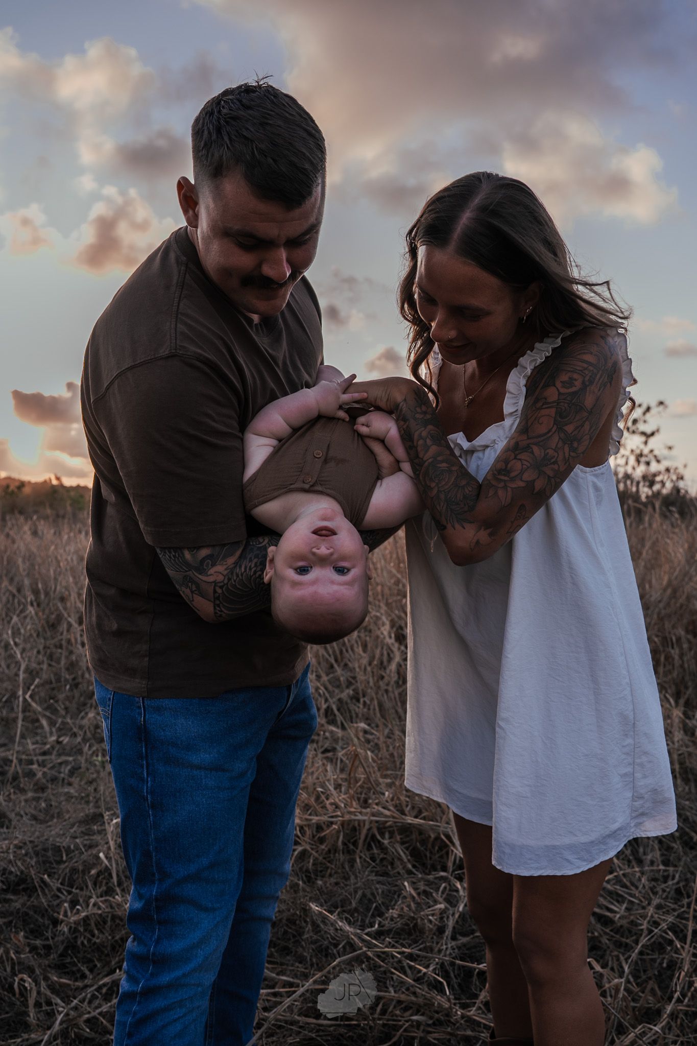 A couple embraces tenderly during a sunset photoshoot in a rustic outdoor setting.