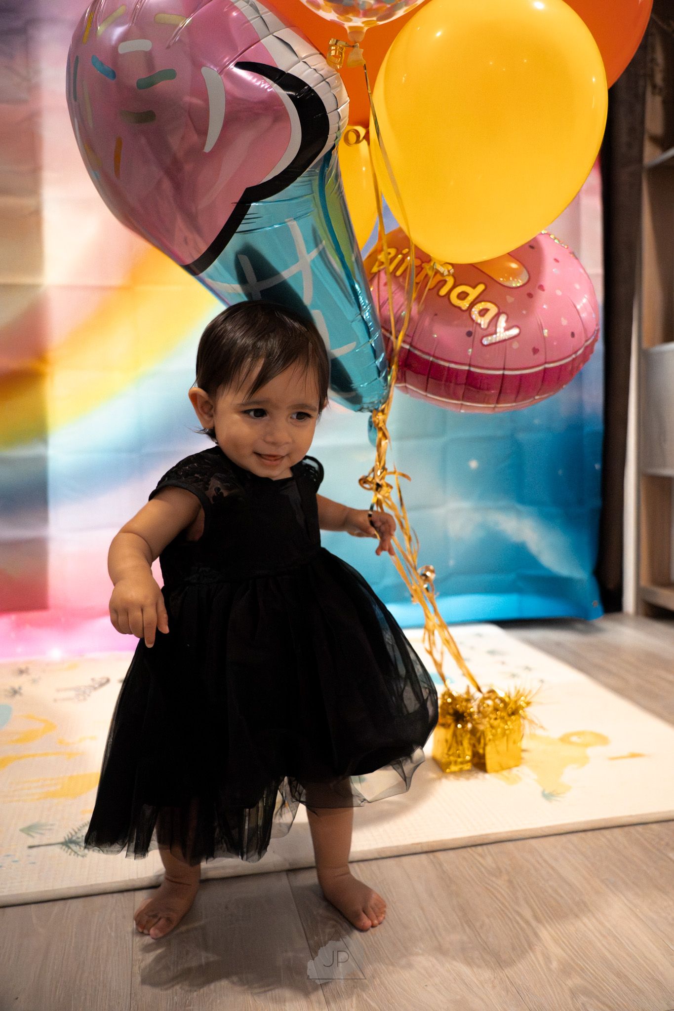 A series of candid shots capturing a toddler in a black dress playing with pink and yellow birthday balloons.