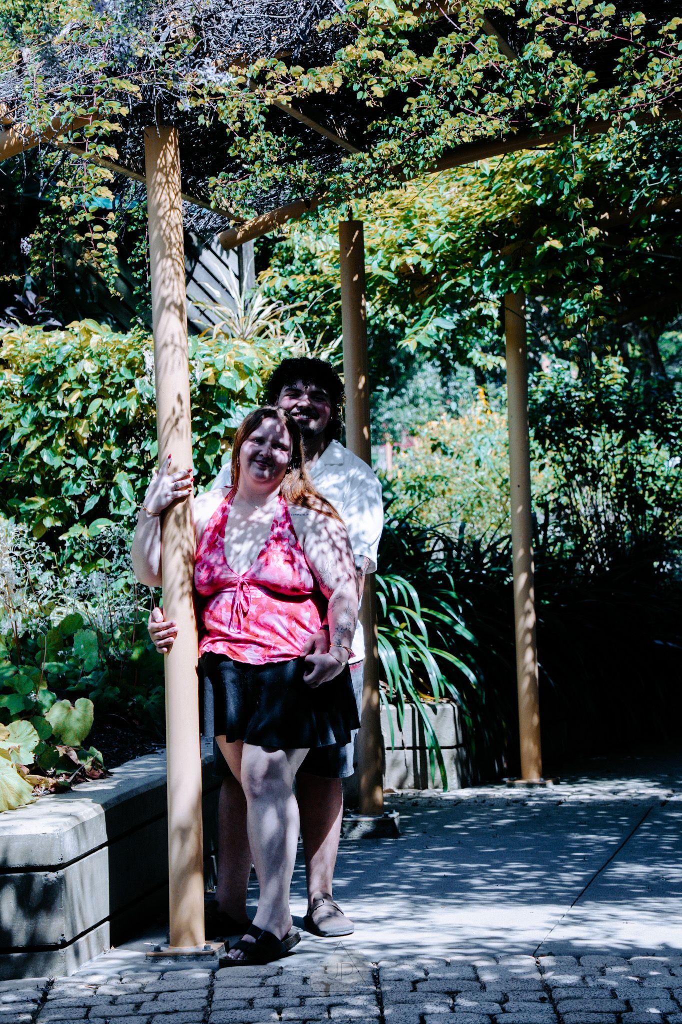 A sequence of four photos showing a couple walking along a stone pathway surrounded by lush garden foliage on a sunny day.