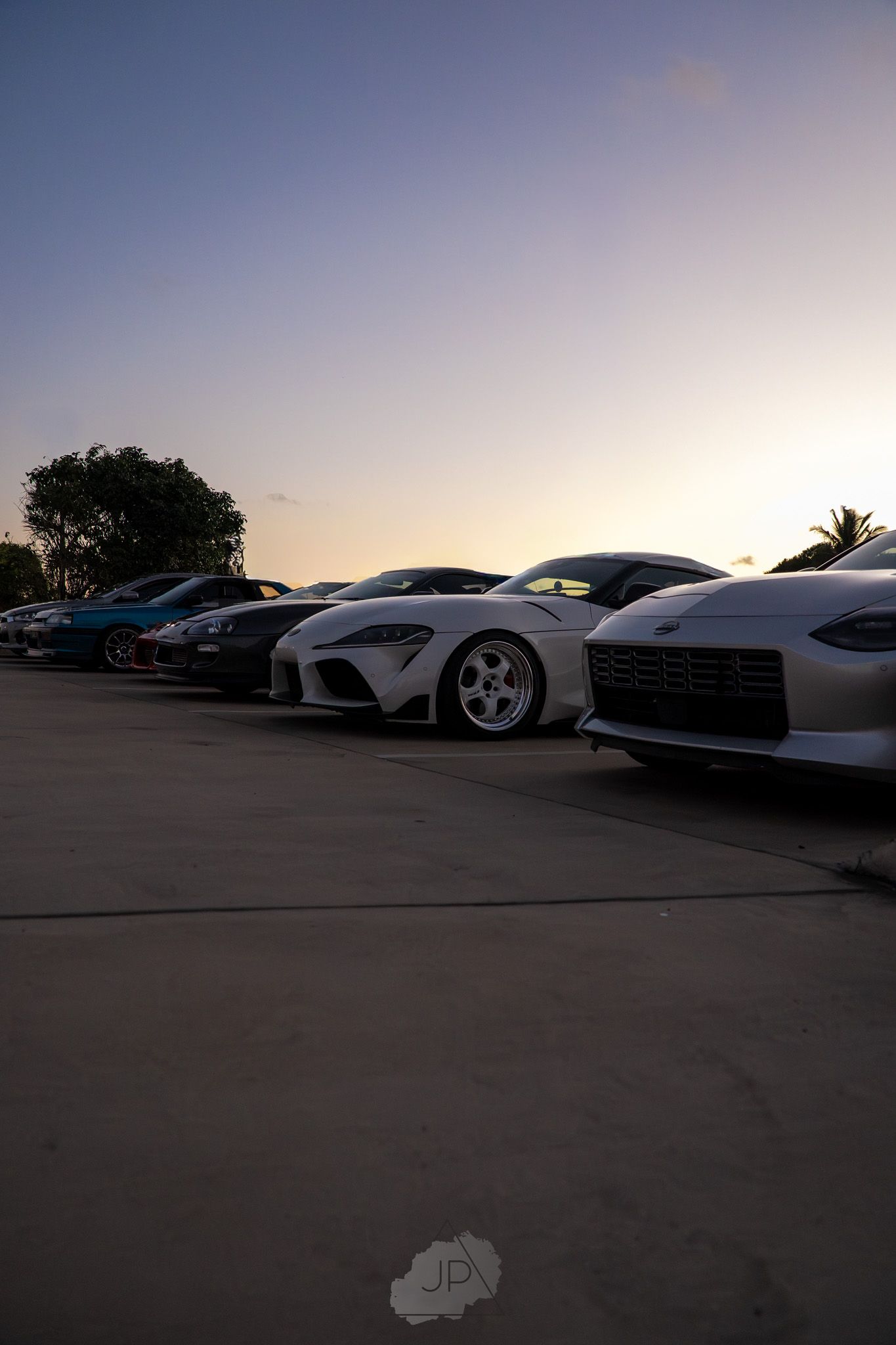Row of luxury sports cars parked at sunset silhouetted against a purple dusk sky.