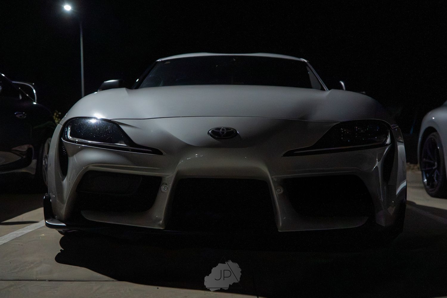 Dark front view silhouette of a modern sports car with dramatic lighting showing its sleek body lines.