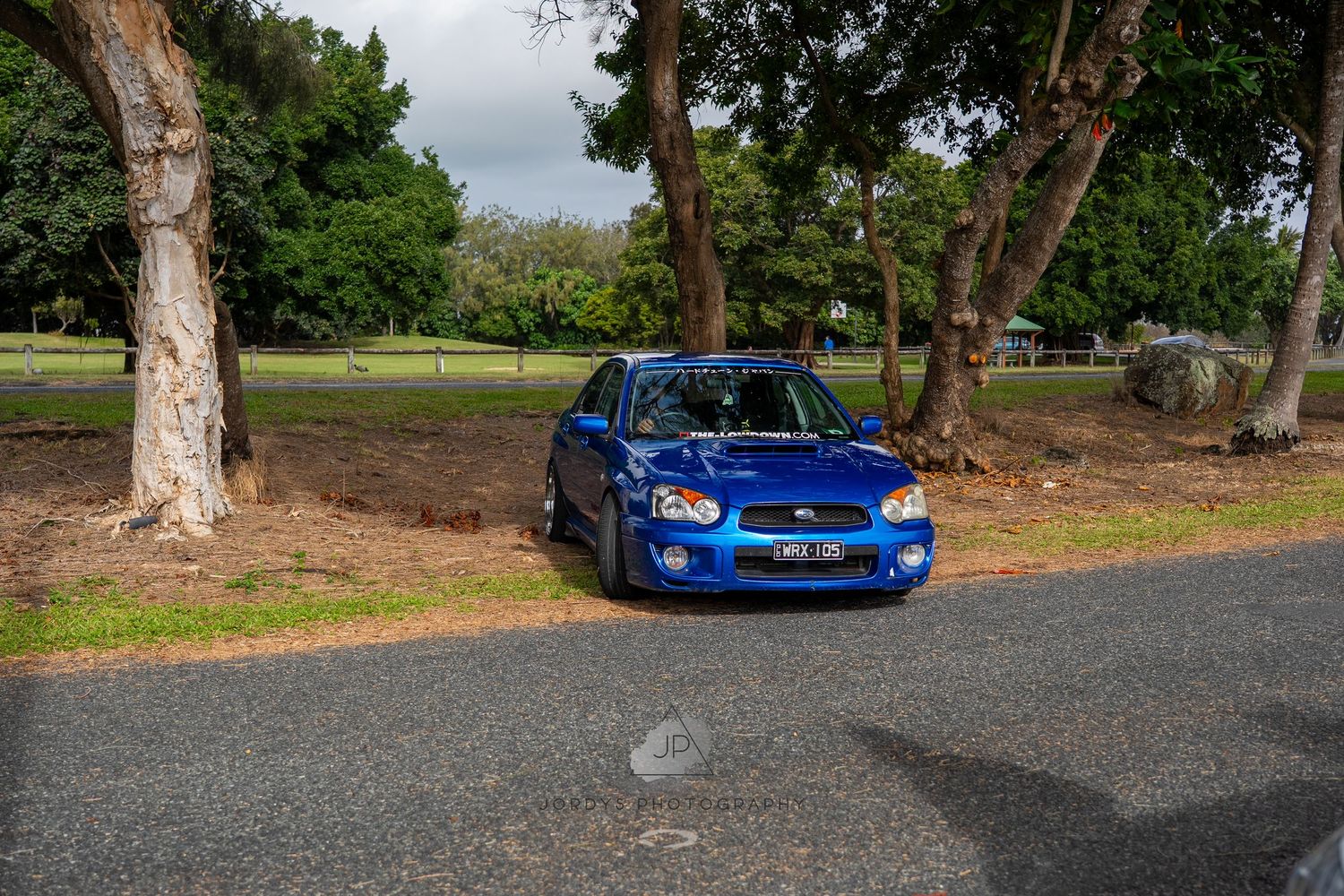 Blue Subaru WRX parked near trees on a gravel path shows off its sporty rally-inspired styling.