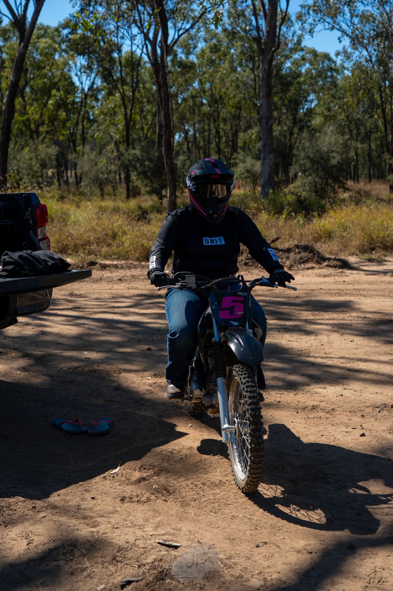 Dirt bike rider in protective gear navigates a dusty trail through Australian bushland on a sunny day.