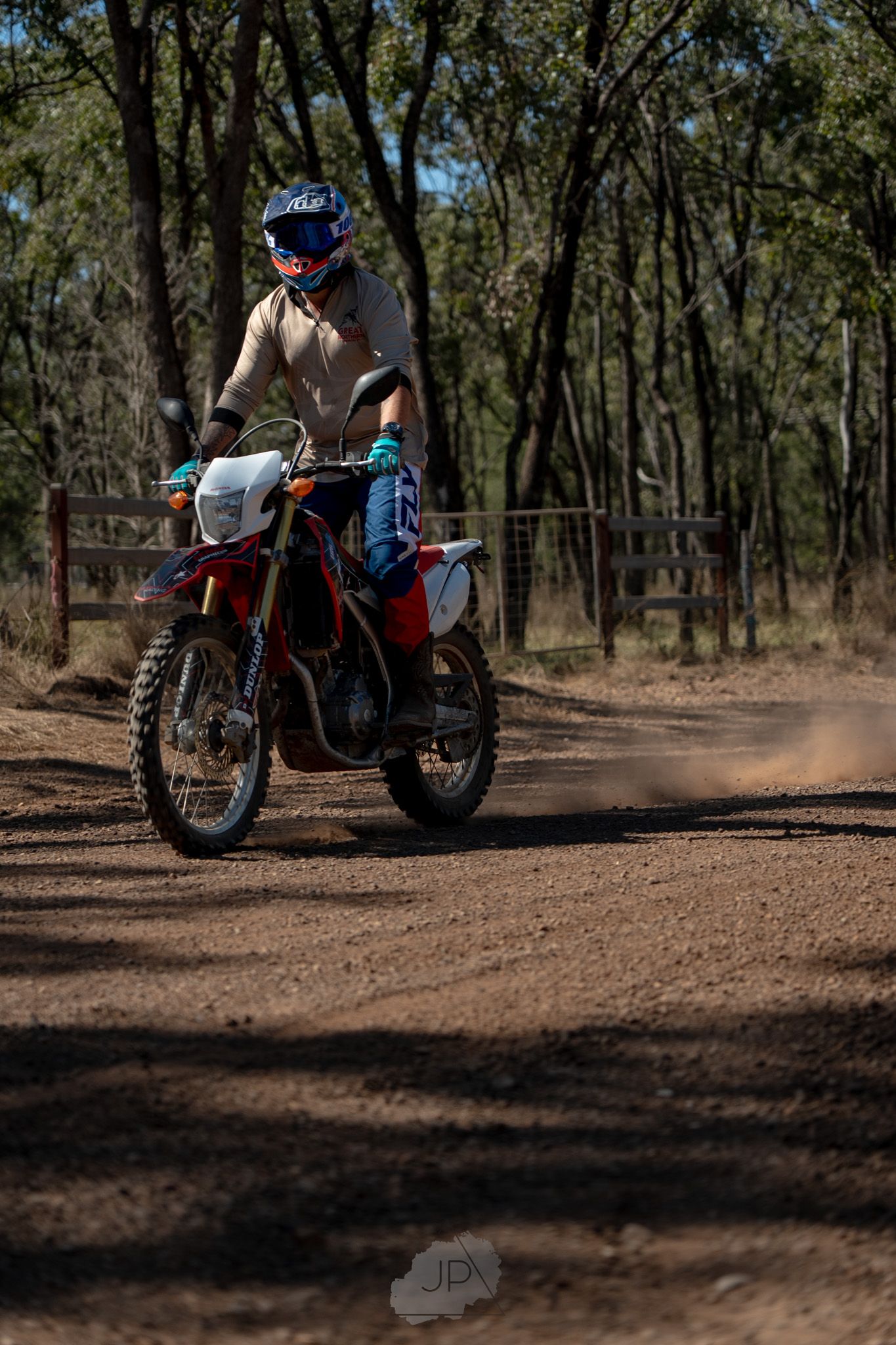 A dirt bike rider kicks up dust while navigating a winding forest trail during an off-road motorcycle adventure.