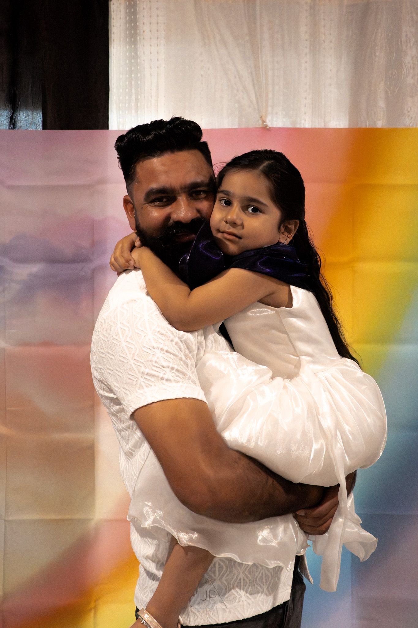 Series of photos showing a warm embrace between two people wearing white against a colorful background.