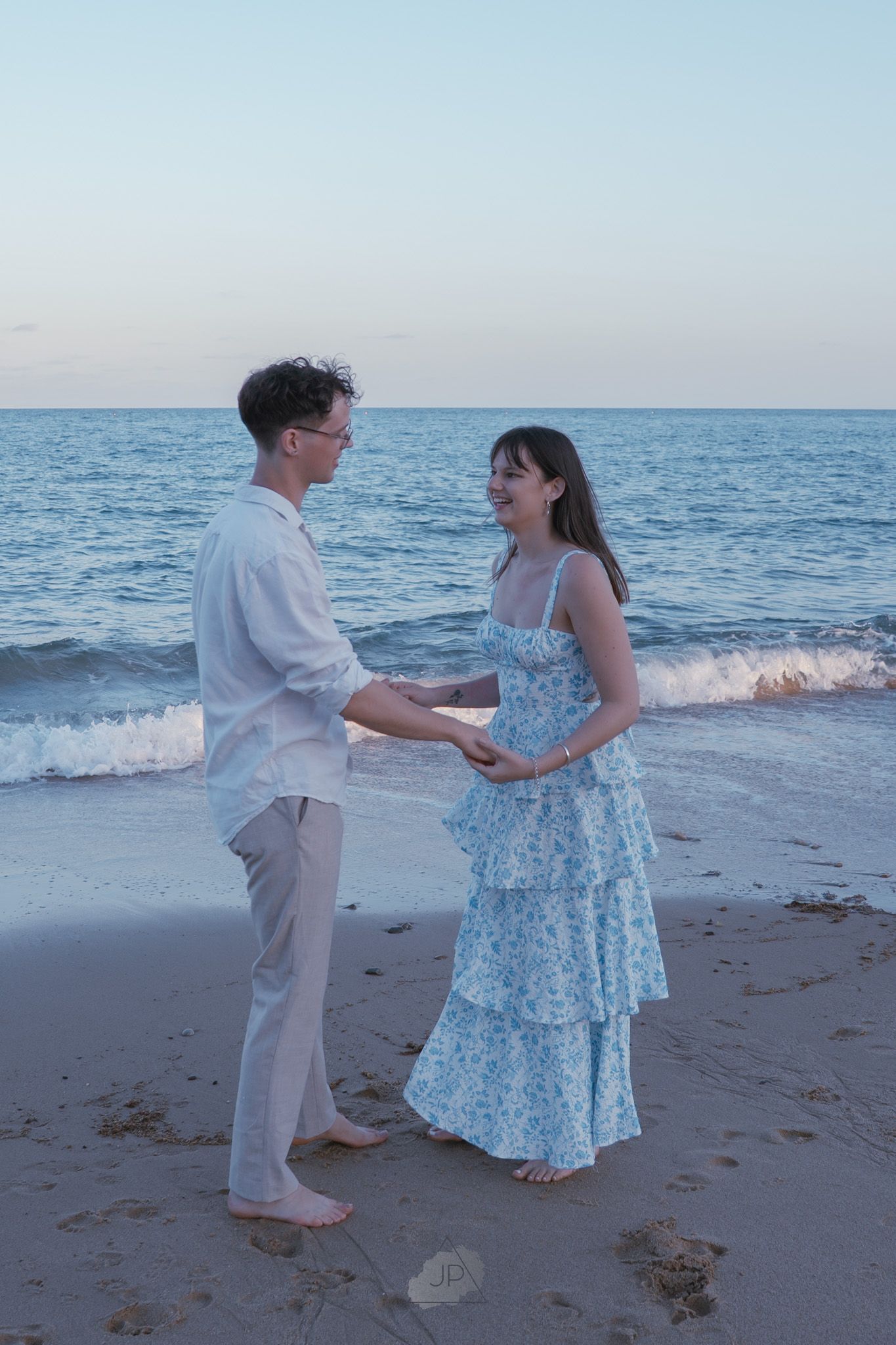 Two people dance together at sunset on a sandy beach with ocean waves in the background.