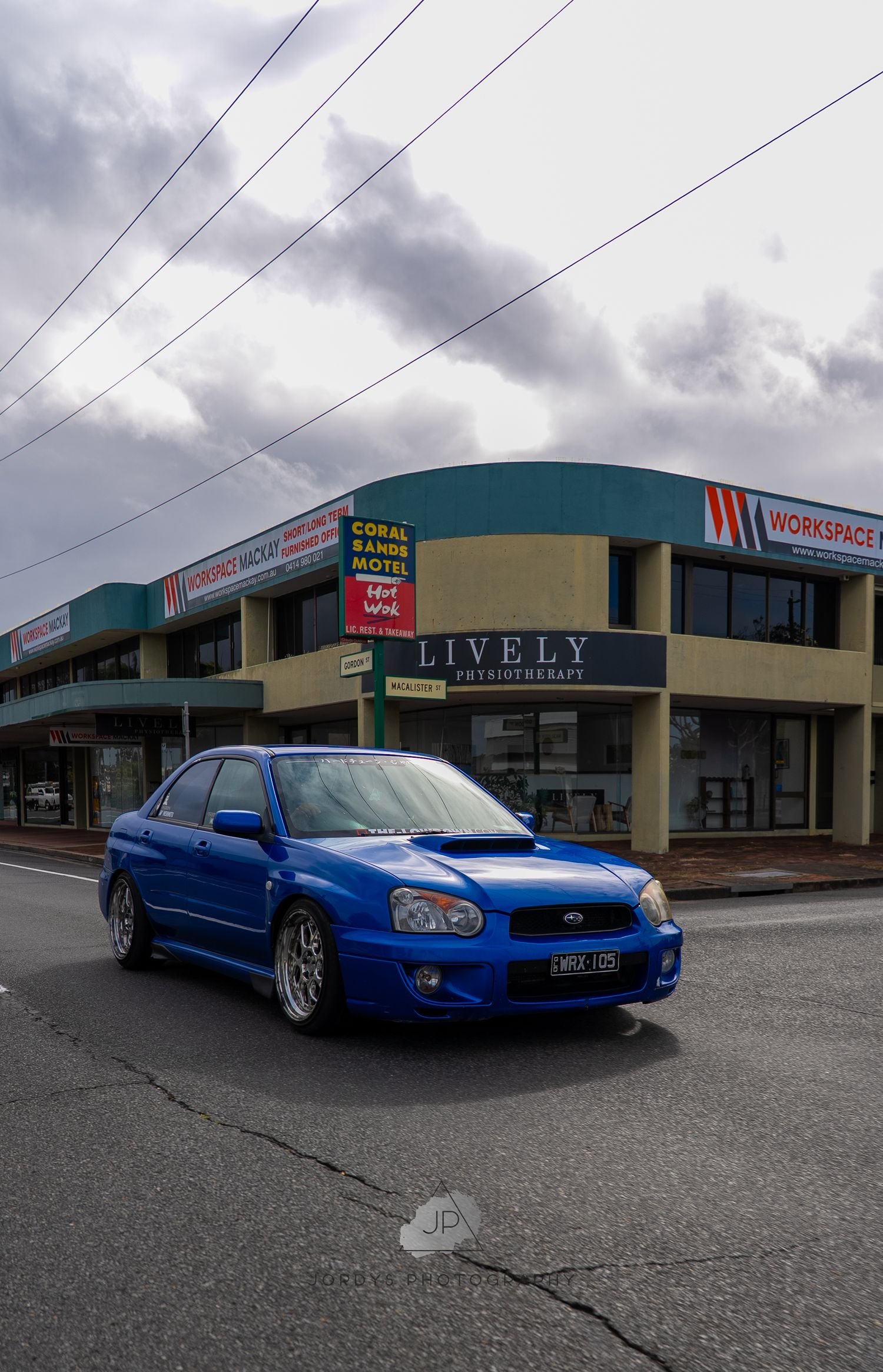 A bright blue Subaru WRX STI is parked in front of a strip mall on an overcast day.