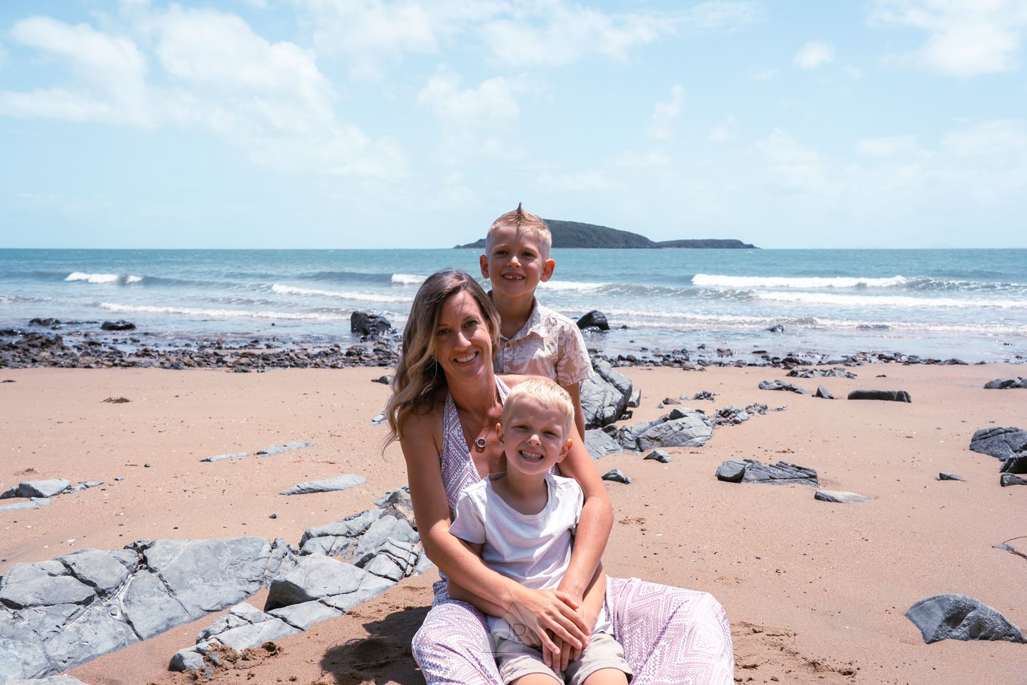 People enjoying a sunny day at a scenic beach with waves and rocky coastline in the background.