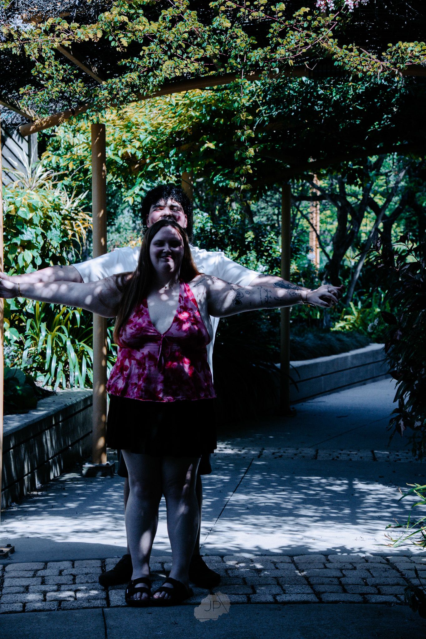 A person in dark clothing and floral print strikes expressive poses on a stone pathway surrounded by lush greenery.