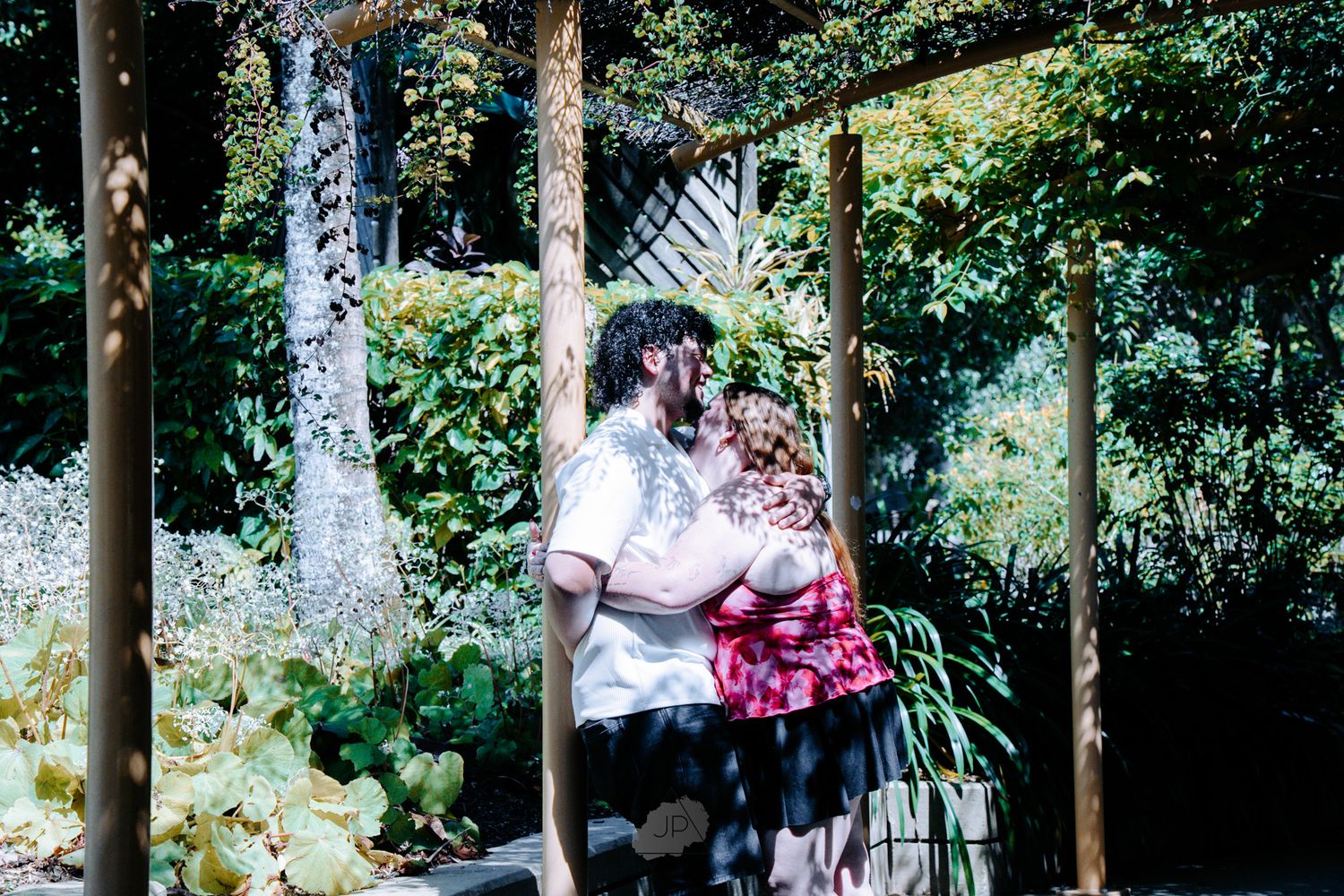 Couple embraces and dances together in a lush green forest setting with sunlight filtering through the trees.