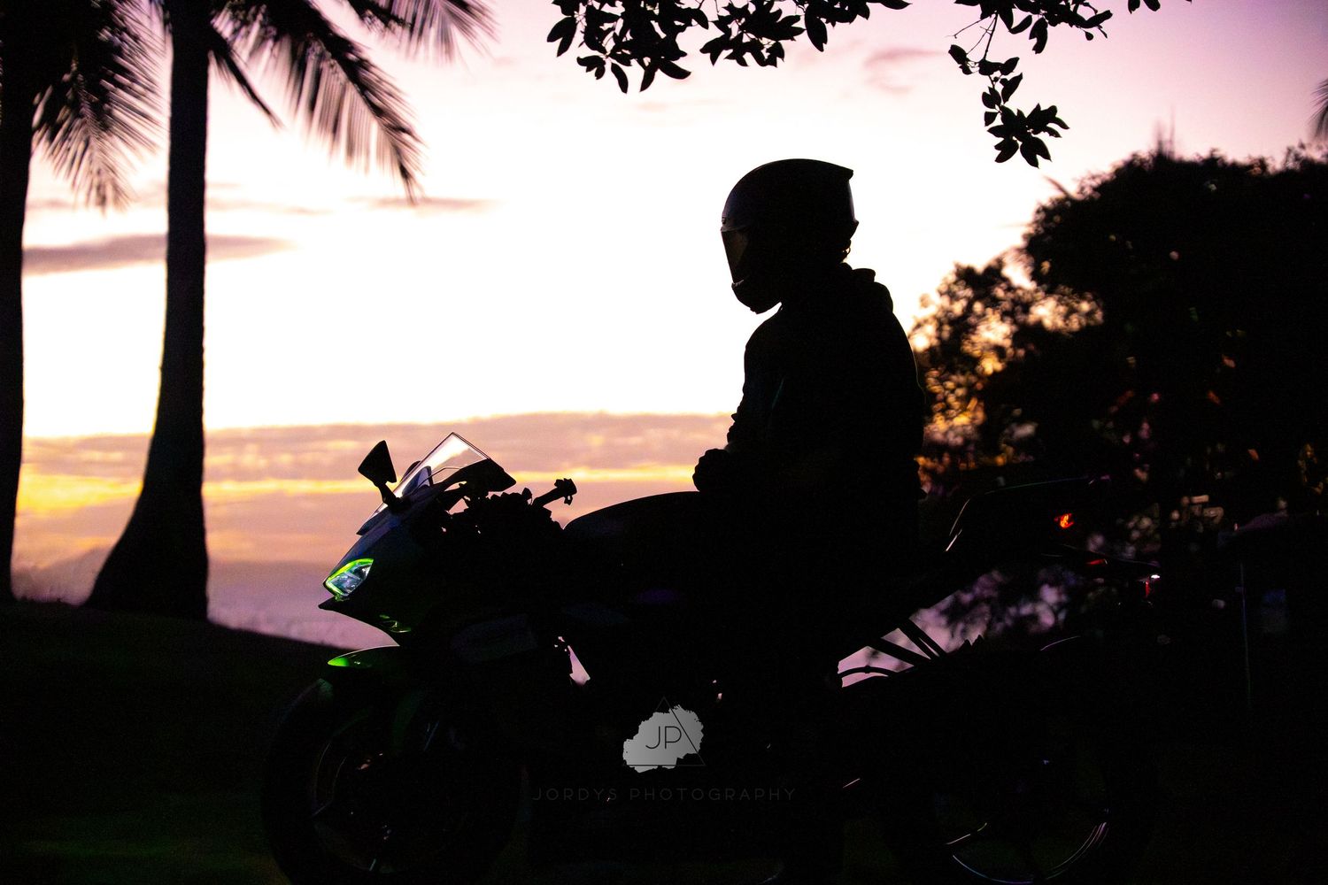 Silhouettes of palm trees against a vibrant purple sunset sky create a serene tropical scene.