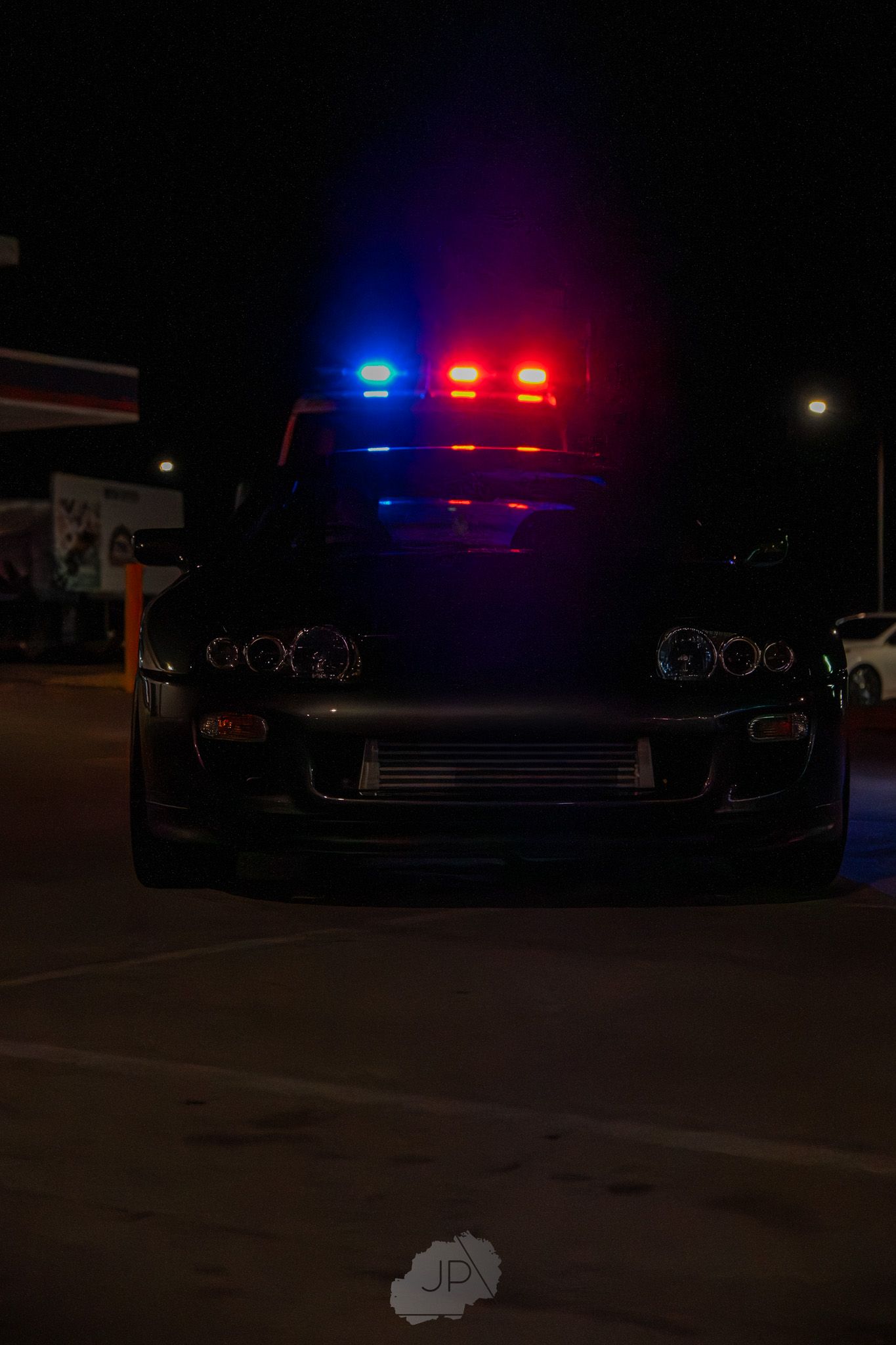 Police car flashing lights illuminate dark parking lot at night.