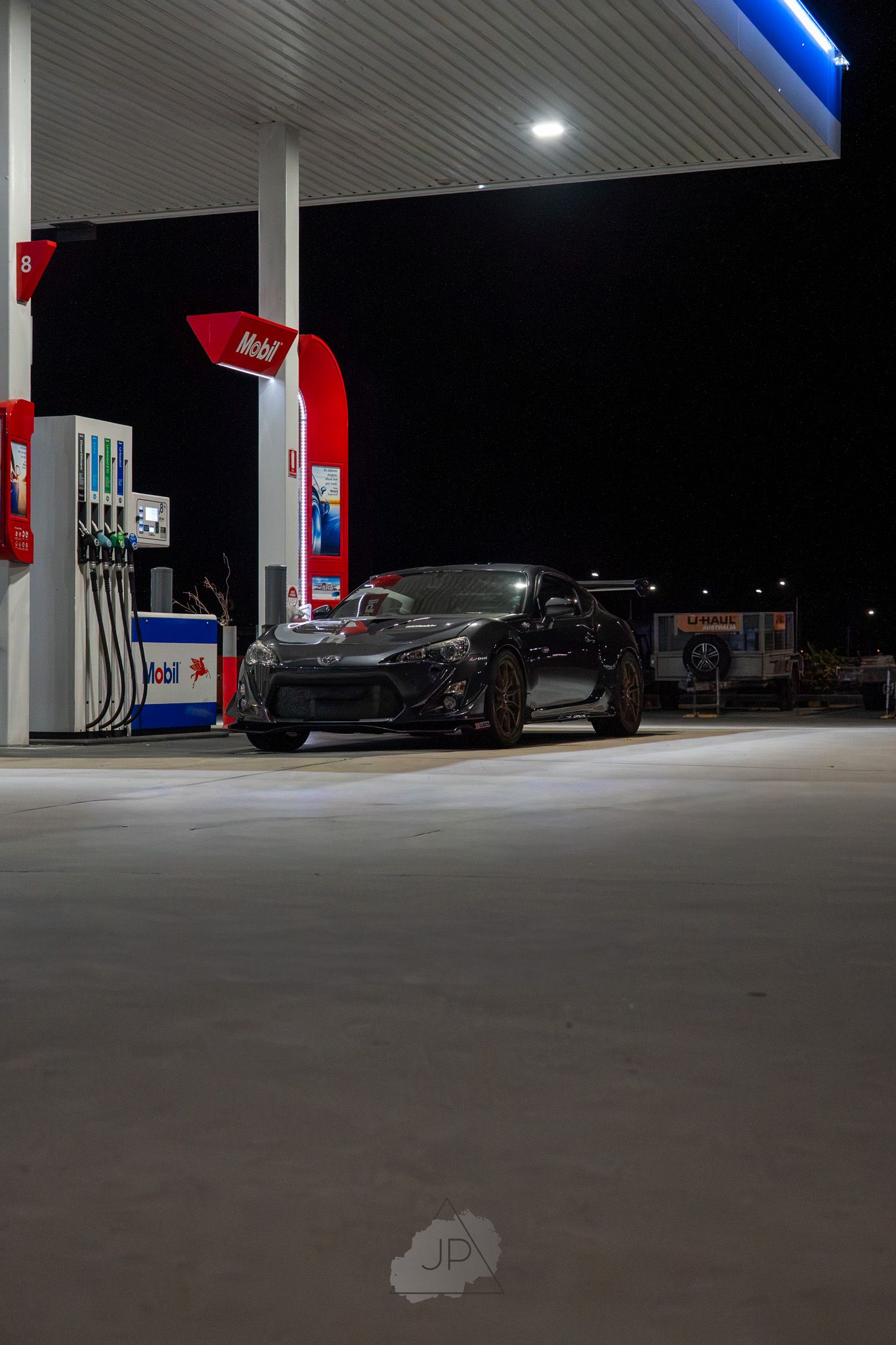 Illuminated gas station at night with empty fuel pumps and concrete floor visible under bright overhead lighting.