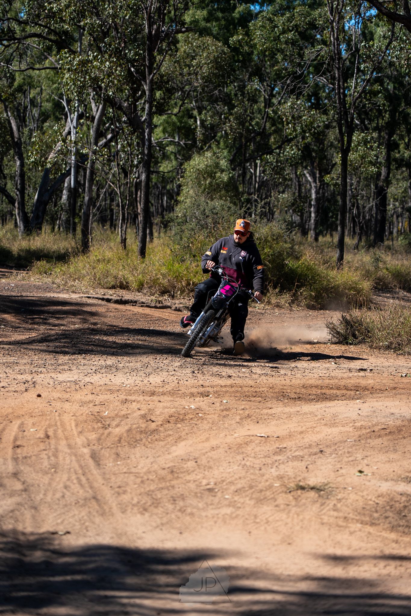 Mountain biker navigates a dusty dirt trail curve through eucalyptus trees in an Australian forest.