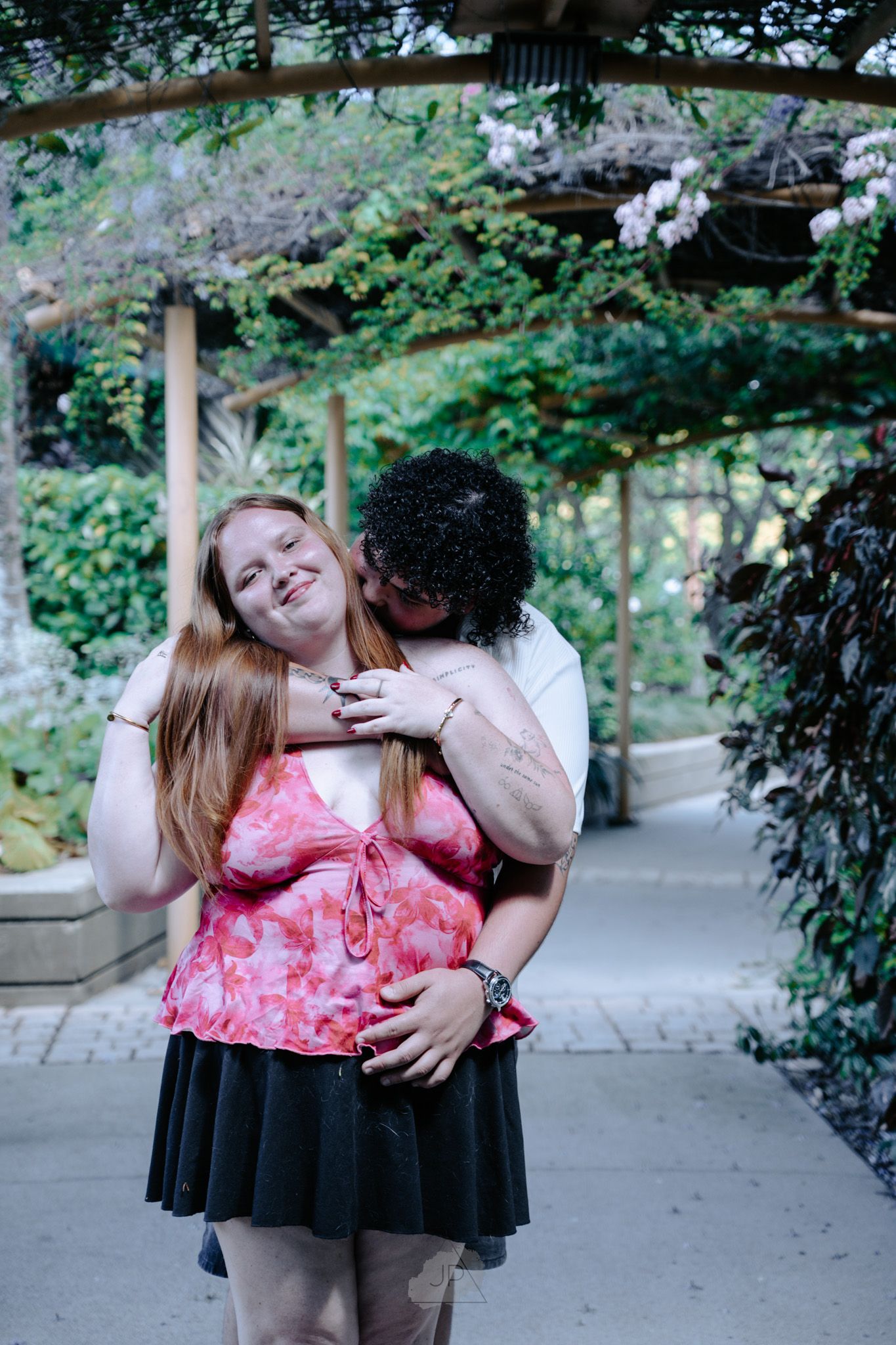 A couple shares tender moments together in a park setting wearing pink and black outfits.