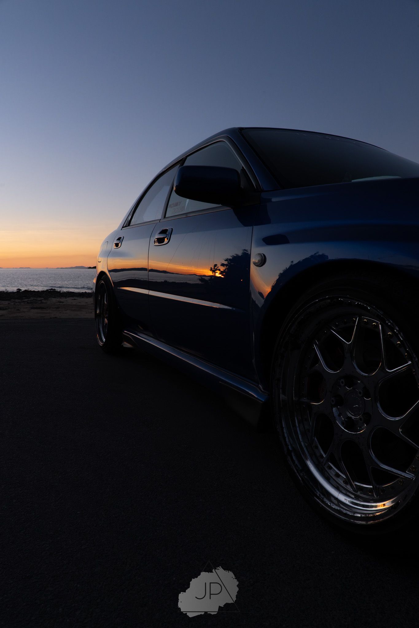 A row of modified JDM cars silhouetted against a dusky sunset sky with dark moody lighting.