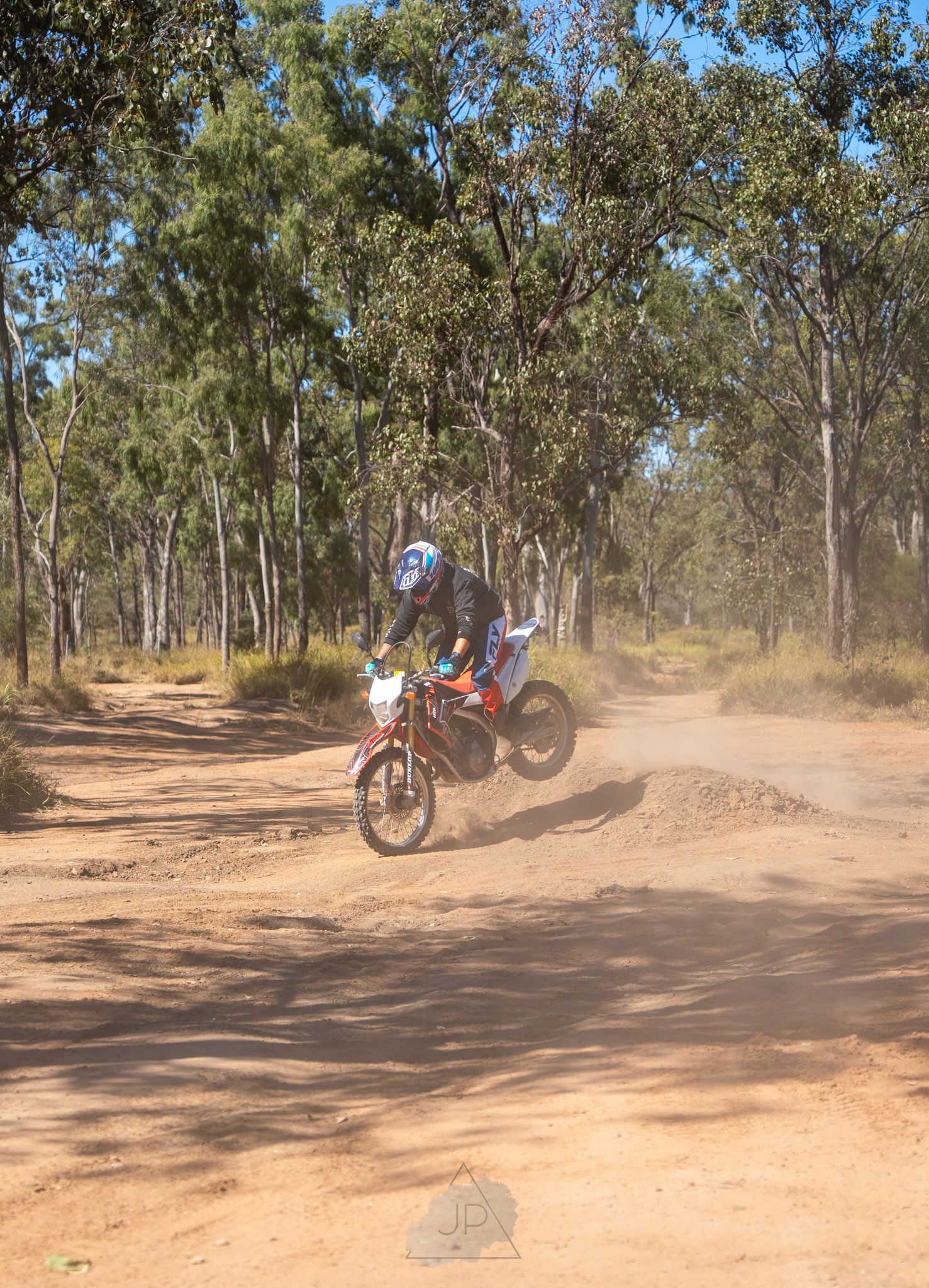 Dirt bike rider jumps over dusty track through Australian bushland on a red motorcycle.