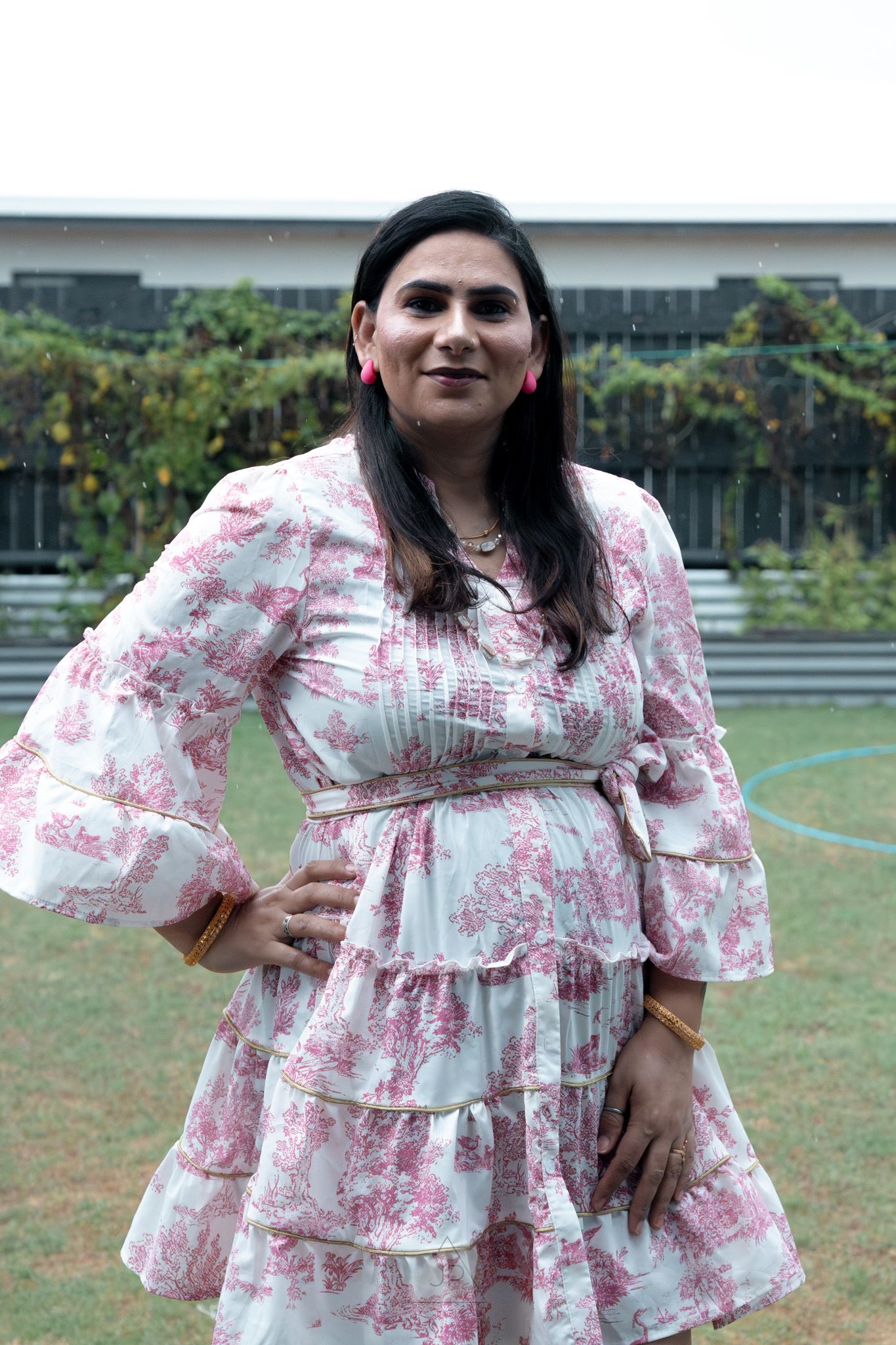 A woman poses outdoors in a pink and white floral dress with ruffled sleeves against a grassy background.