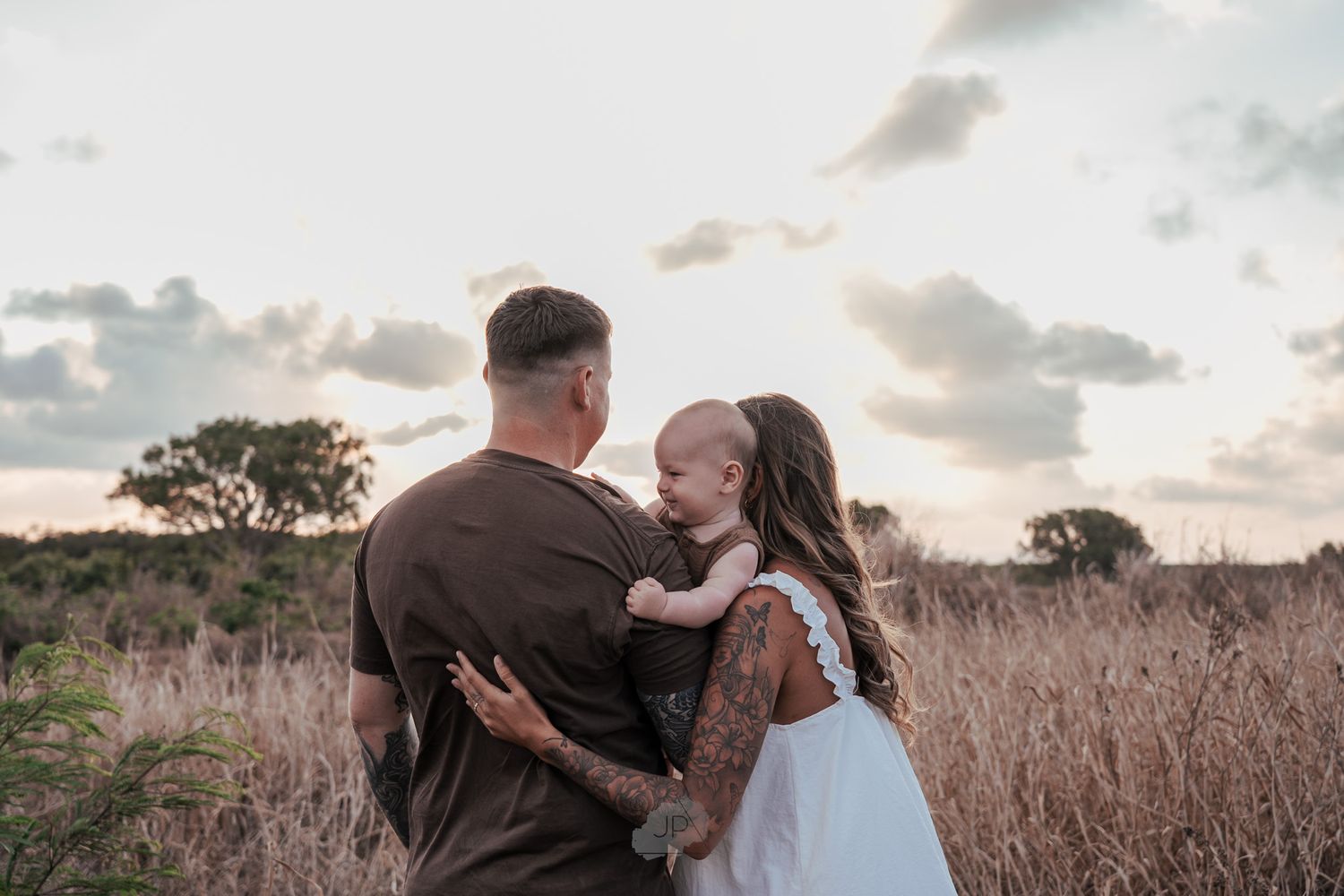 A couple shares a romantic embrace in a golden field during sunset while taking wedding photos.
