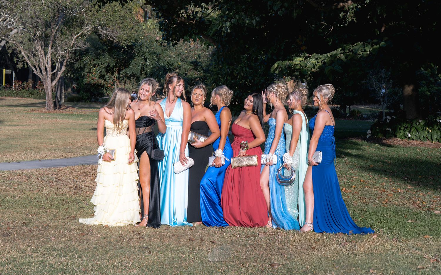 Group of people in formal attire posing together outdoors in a garden setting for a special occasion.