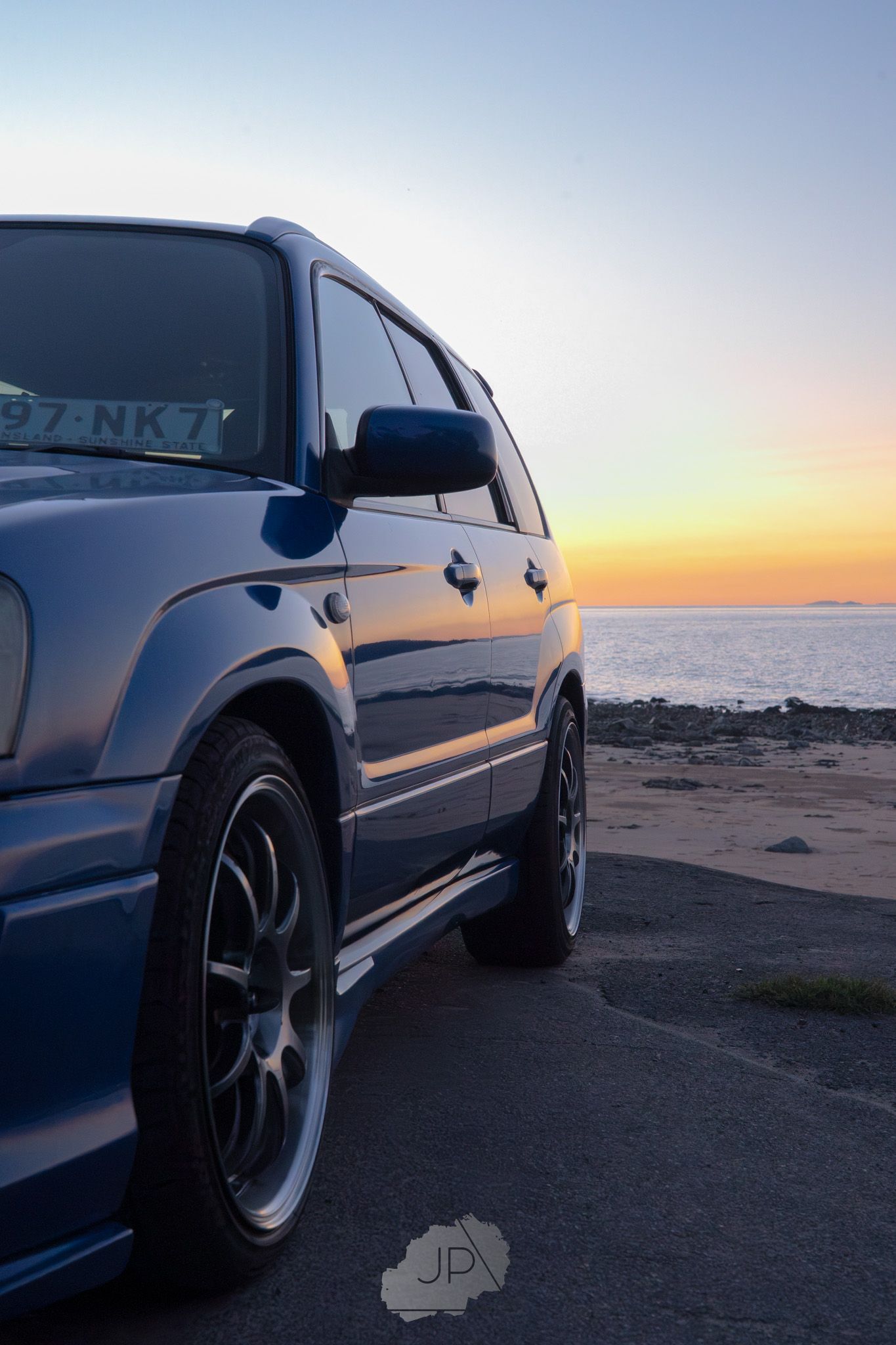 Sleek silver performance vehicle parked on coastal cliffside during a vibrant sunset over the ocean.