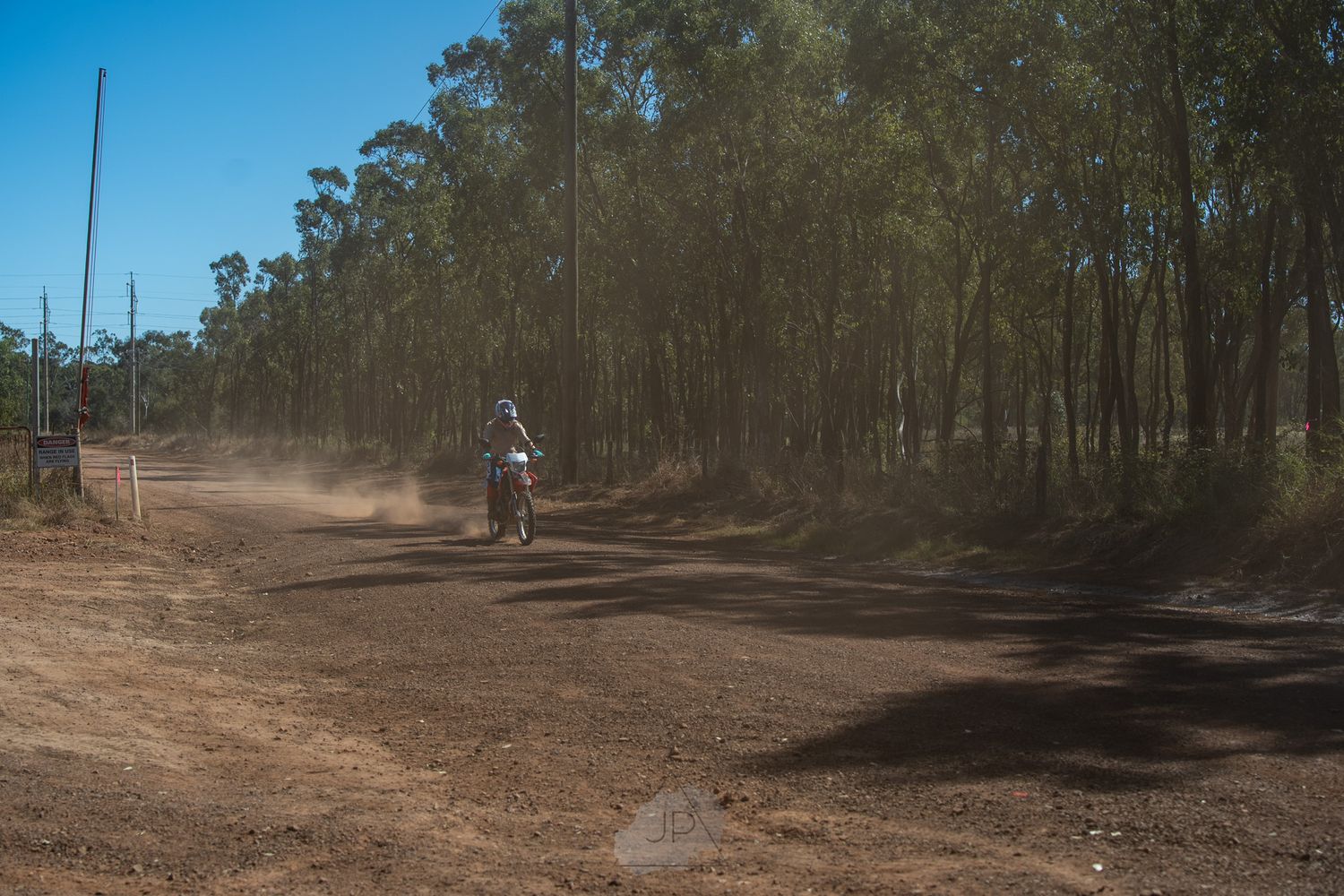 A dirt road winds through an Australian eucalyptus forest landscape with tall trees and dry terrain.