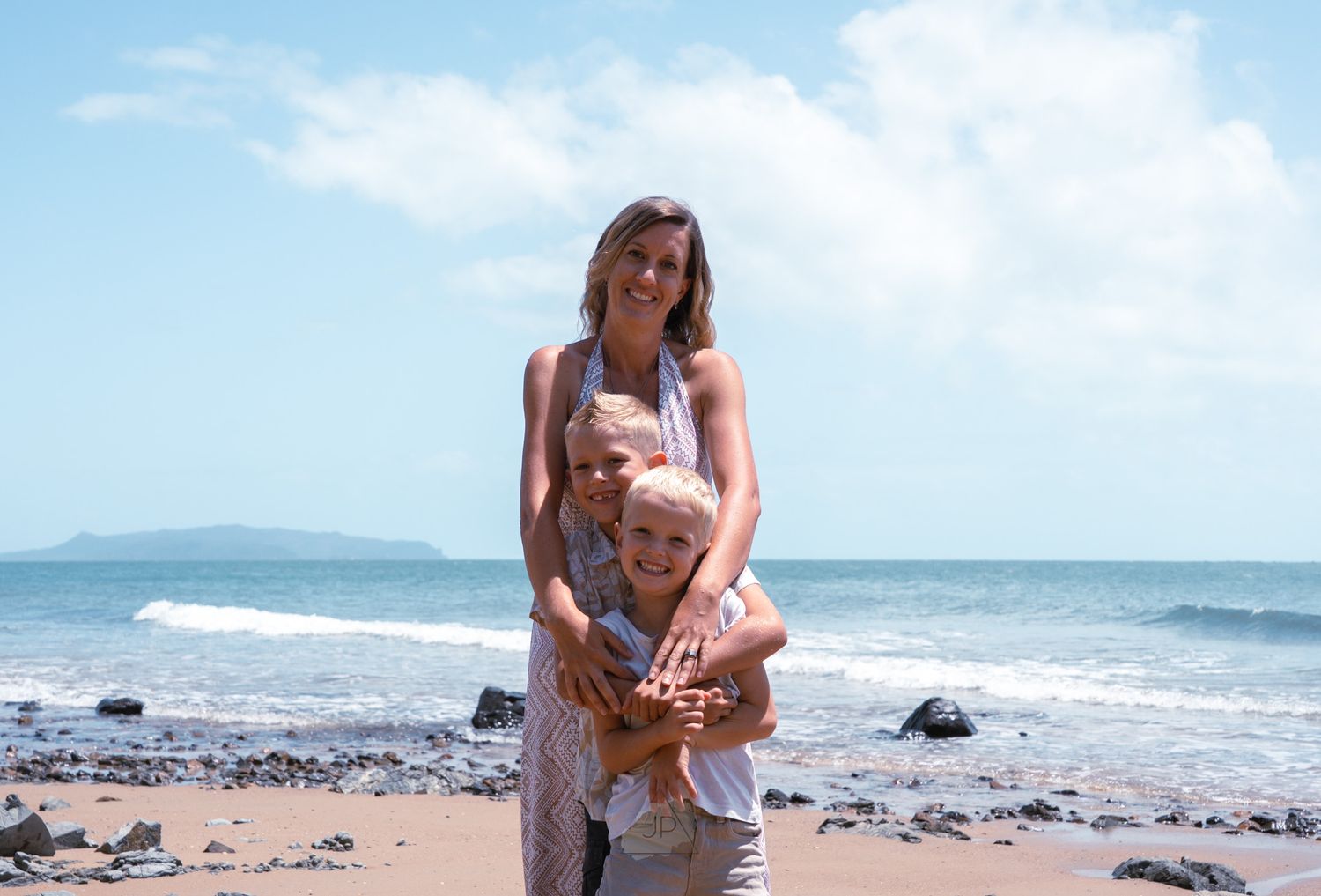 A group of beachgoers enjoy a sunny day along the rocky coastline with waves crashing in the background.