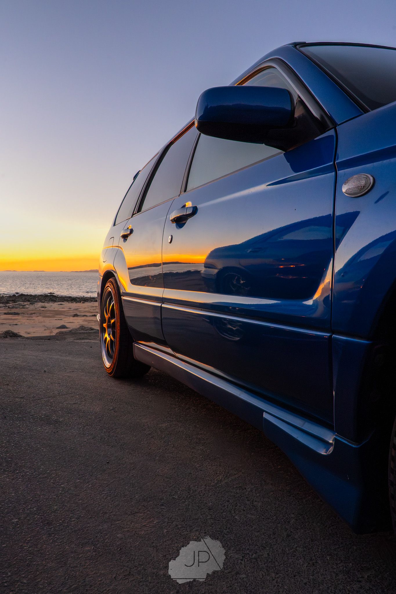 Blue sports car photographed from the side against a vibrant sunset sky.