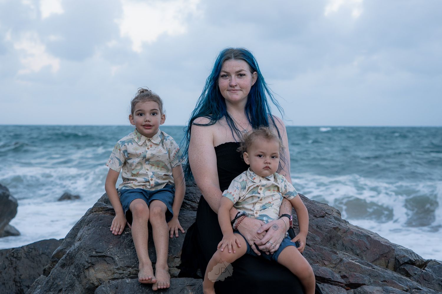 Family enjoying a beach day together while sitting on coastal rocks as waves crash in the background.