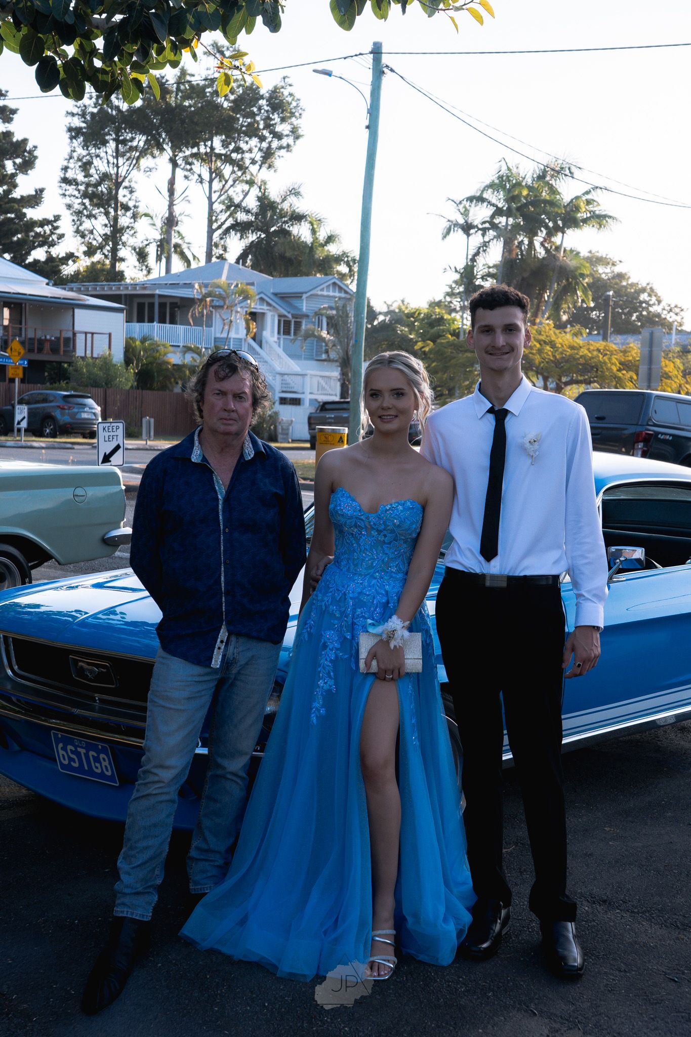 A group poses together in formal attire next to a blue classic car during an evening event.