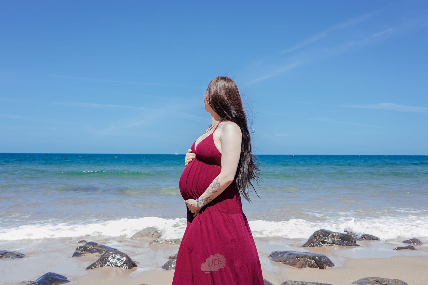 A series of beach photos showing a person in a burgundy dress walking along the shoreline with turquoise waters and rocks.