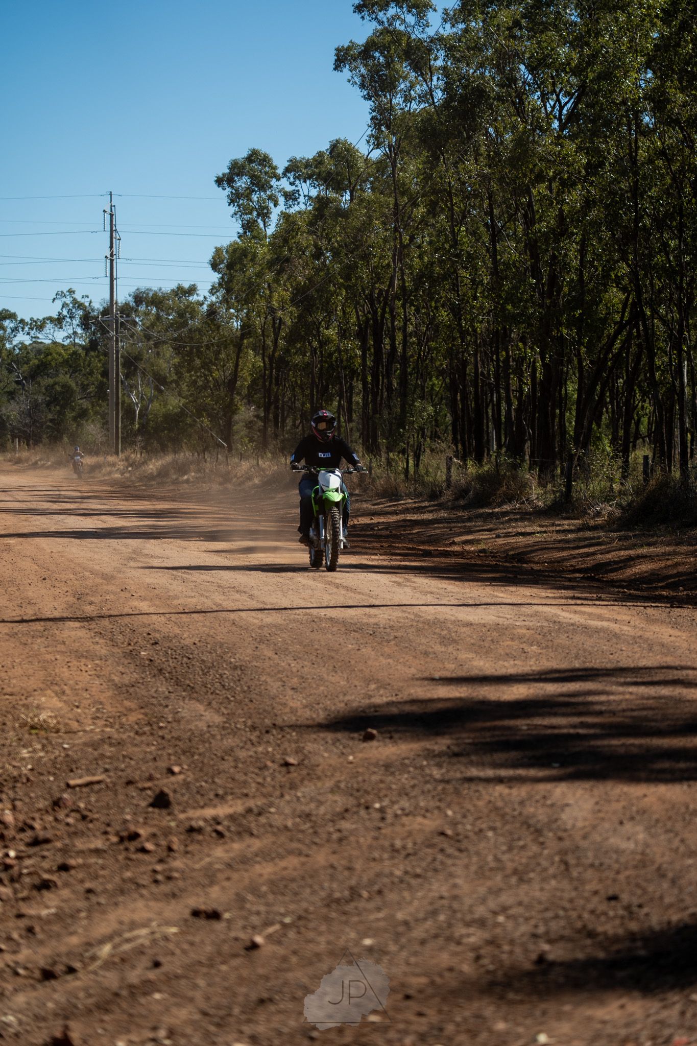 A dirt bike rider traverses a dusty trail through eucalyptus forest in Australia.