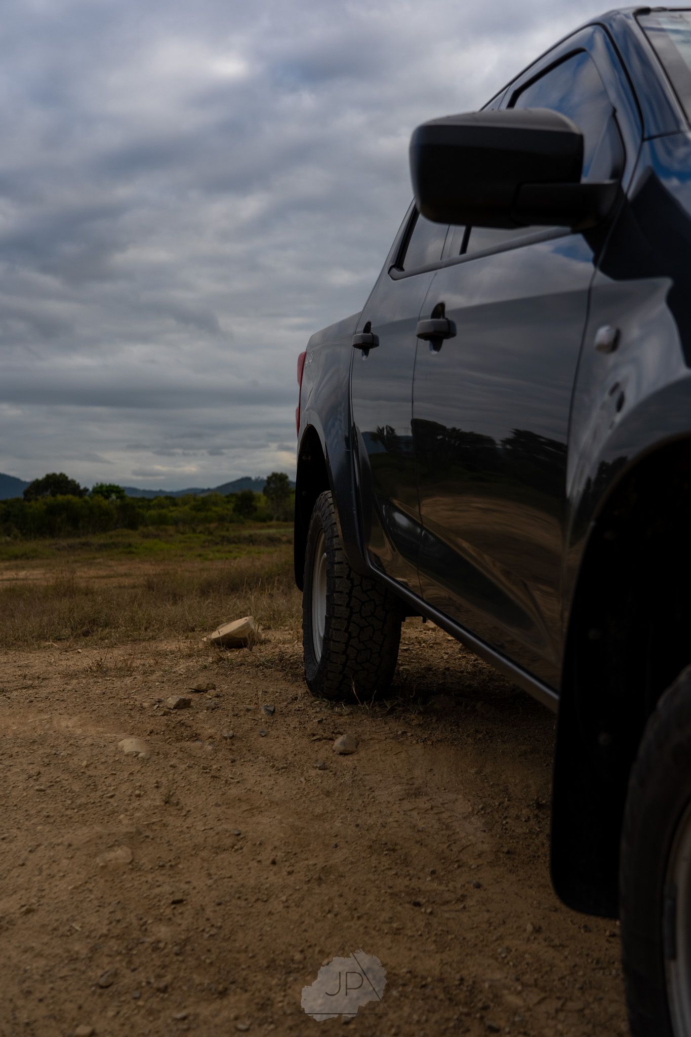 Black pickup truck parked on dusty dirt terrain under cloudy overcast sky, showcasing rear quarter view perspective.