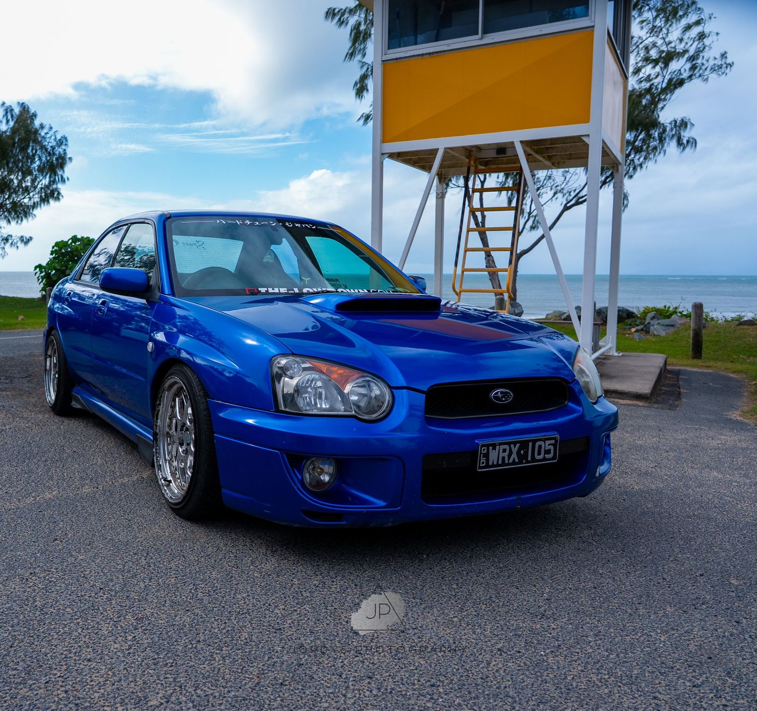 A bright blue Subaru WRX STI sports car parked near the coastline during daytime with scenic ocean views.