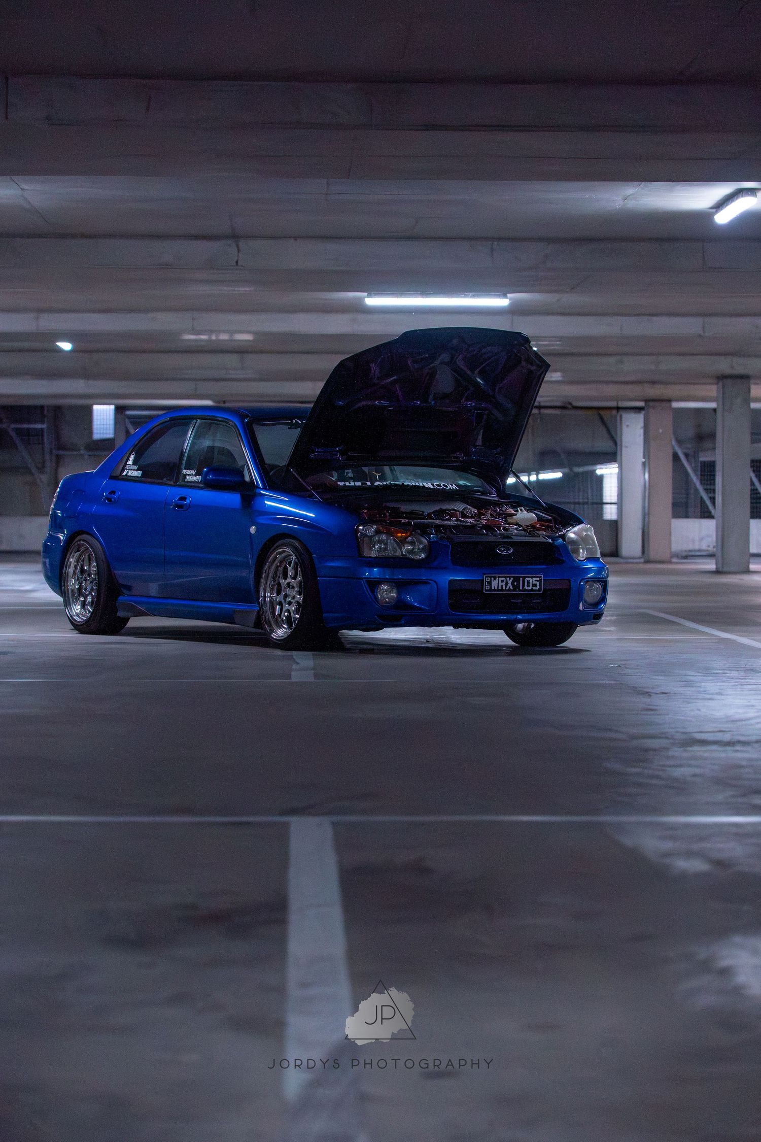 Blue Nissan Silvia sports car with custom modifications parked in a dimly lit concrete parking garage structure.