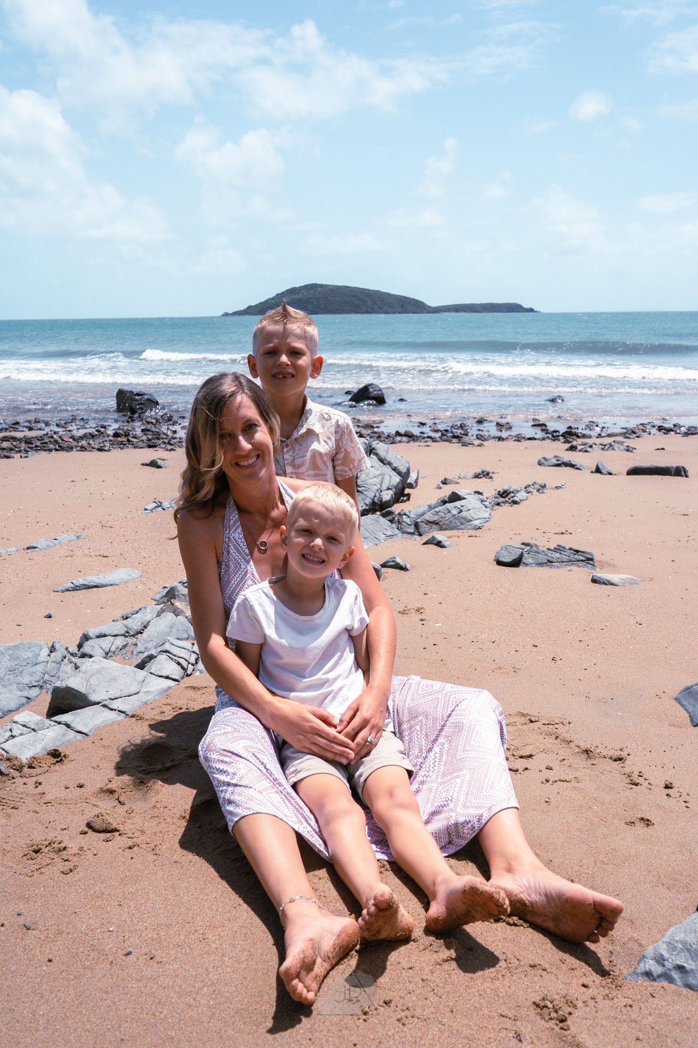 A sunny day at a rocky beach with waves crashing and a distant island visible on the horizon.