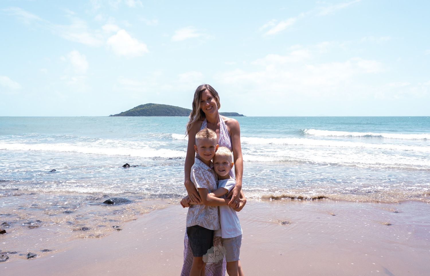 People enjoying a sunny day at a scenic beach with islands visible in the distance and waves rolling onto shore.