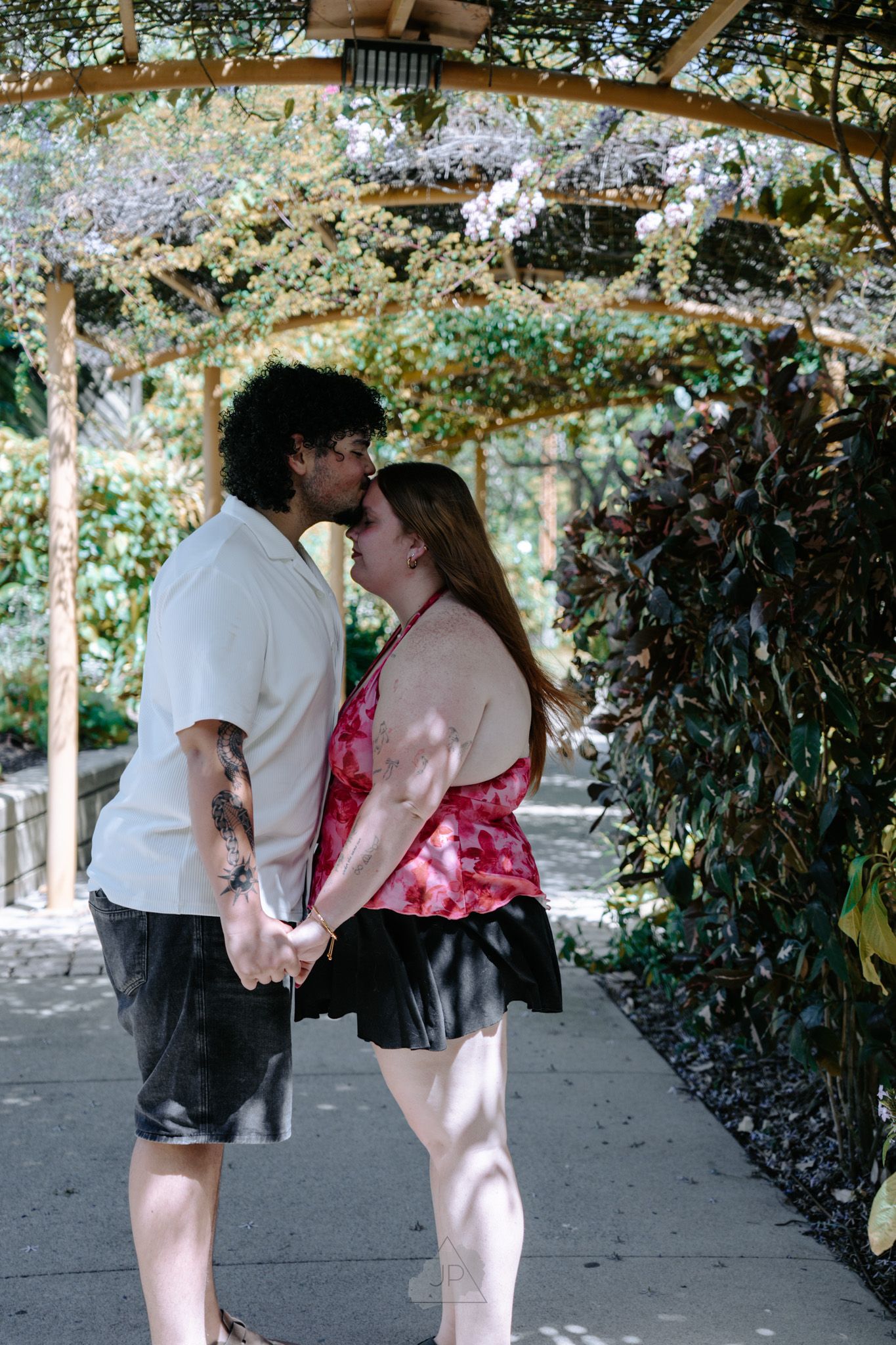 A couple shares a romantic moment under flowering wisteria on a garden path.