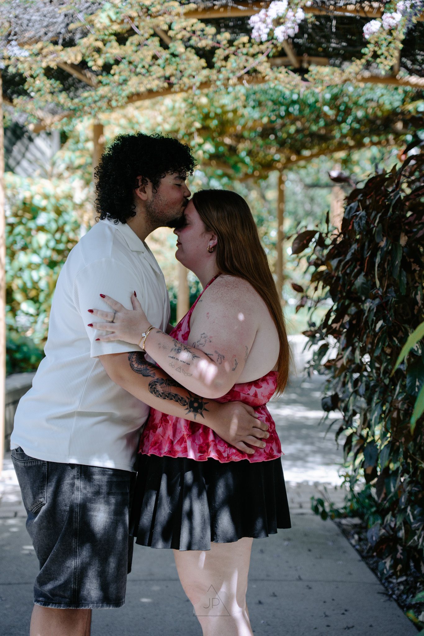 A romantic couple shares tender kisses and embraces in a series of intimate moments under a leafy garden arbor.