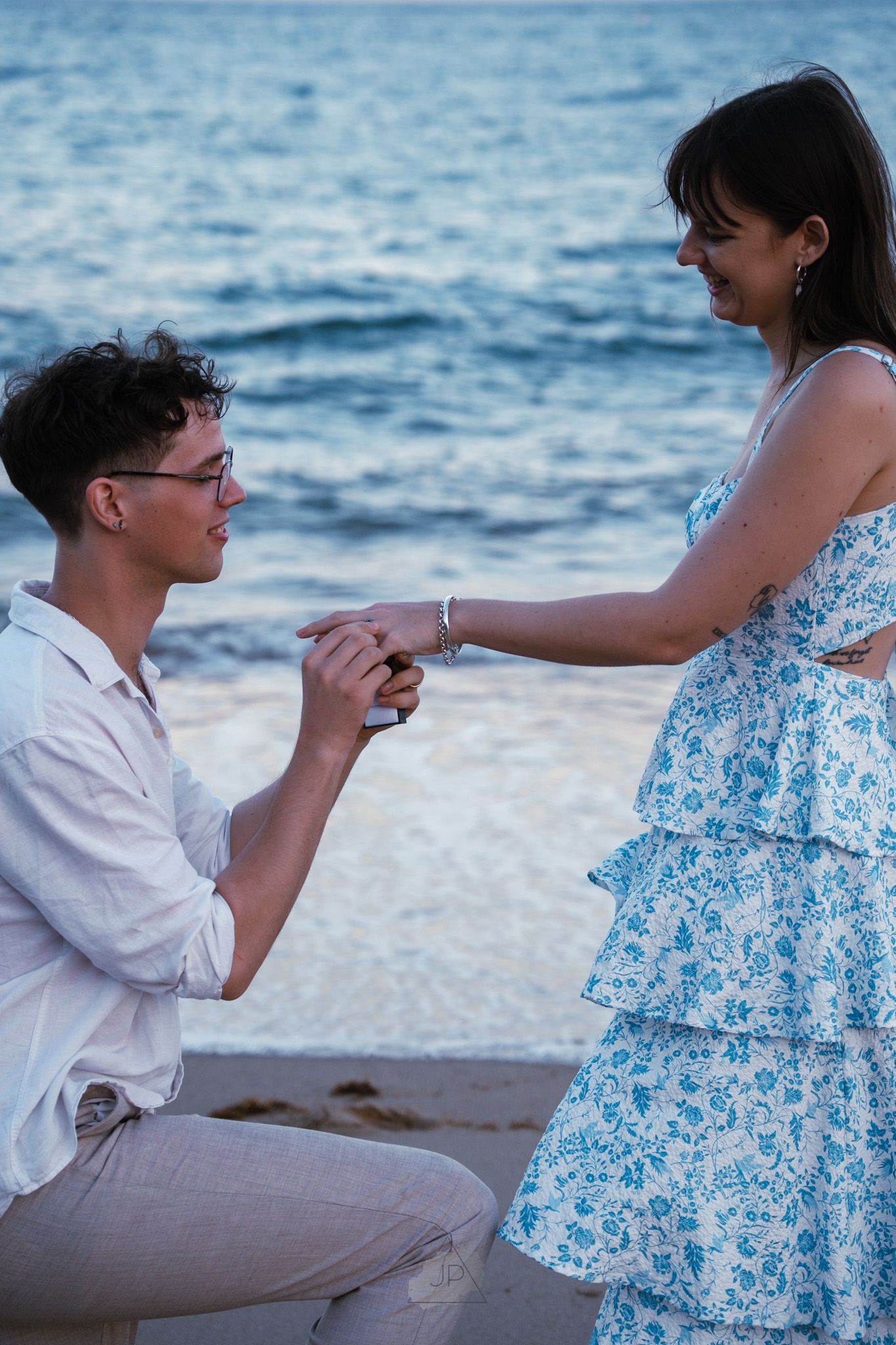 A romantic marriage proposal sequence on a beach at sunset with a floral dress and white shirt.