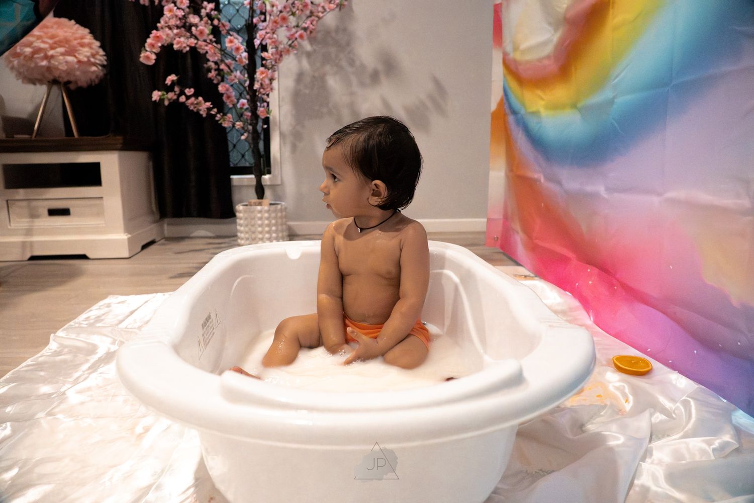 A series of photos showing a baby enjoying bath time in a white tub with colorful rainbow light reflections.