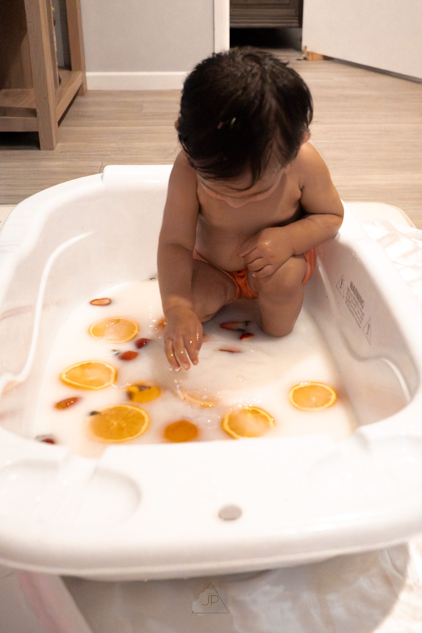 A baby plays with orange circles in a white bathtub during sensory playtime.